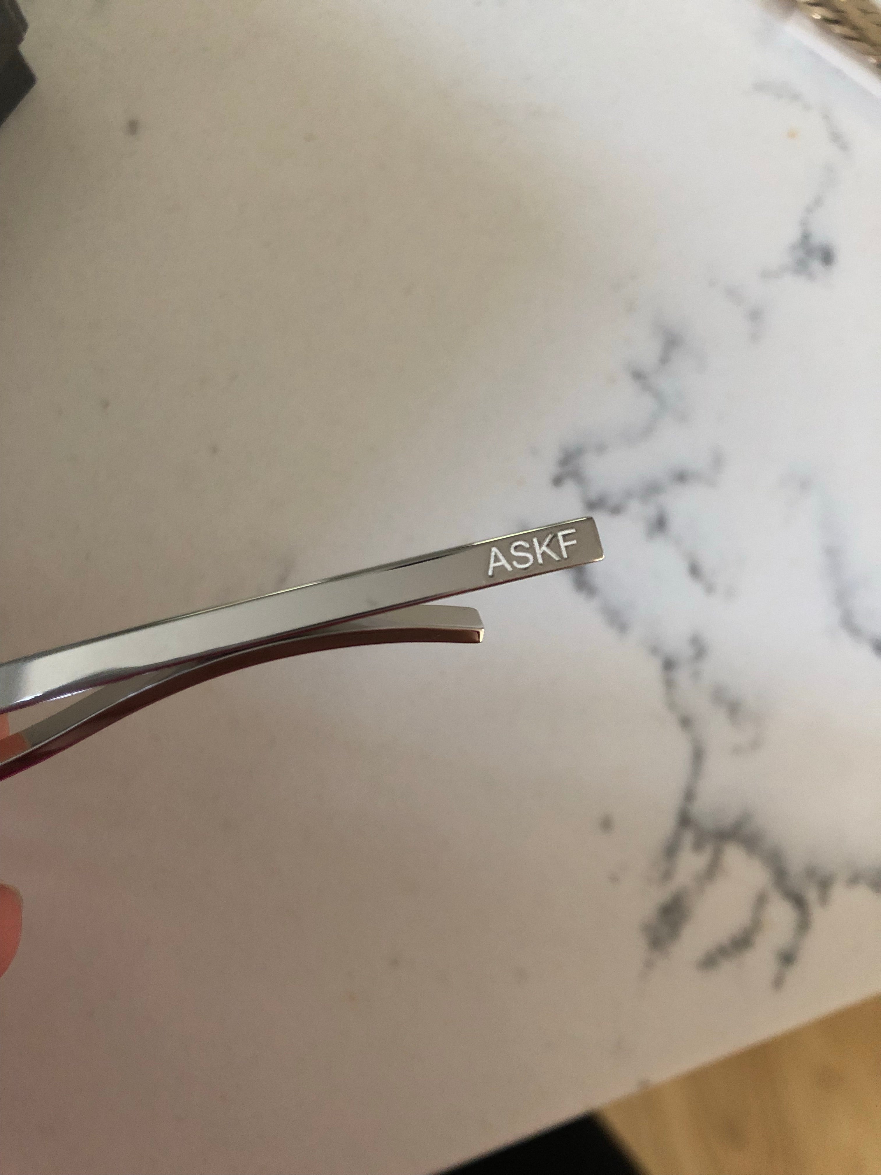 A close-up of an engraved sterling silver triangular tie bar with the initials "ASKF".