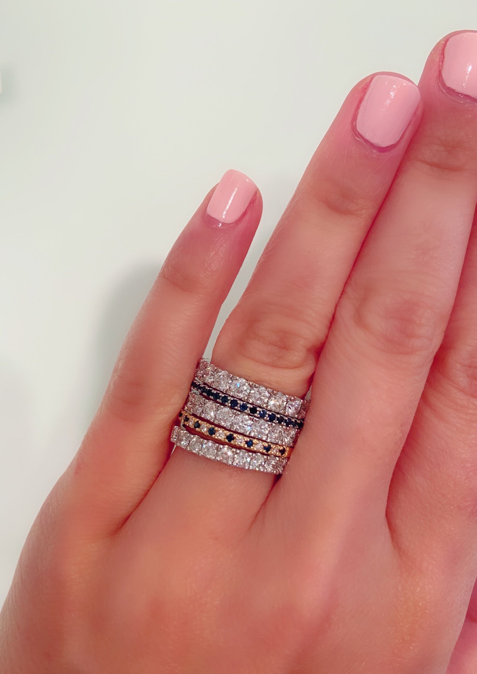 A stack of diamond and birthstone rings on a person's hand against a white background.