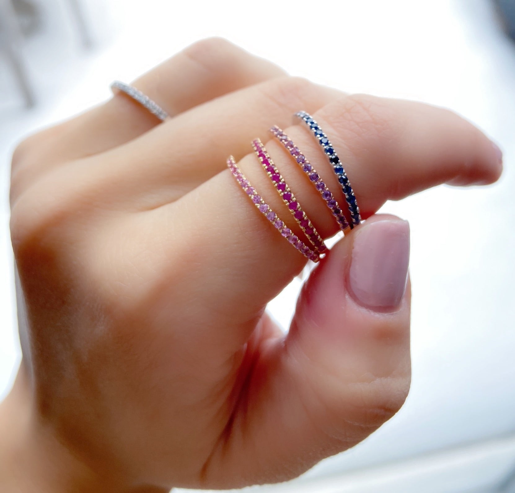 Close-up of a hand wearing a stack of 1.5mm birthstone rings against a white background.
