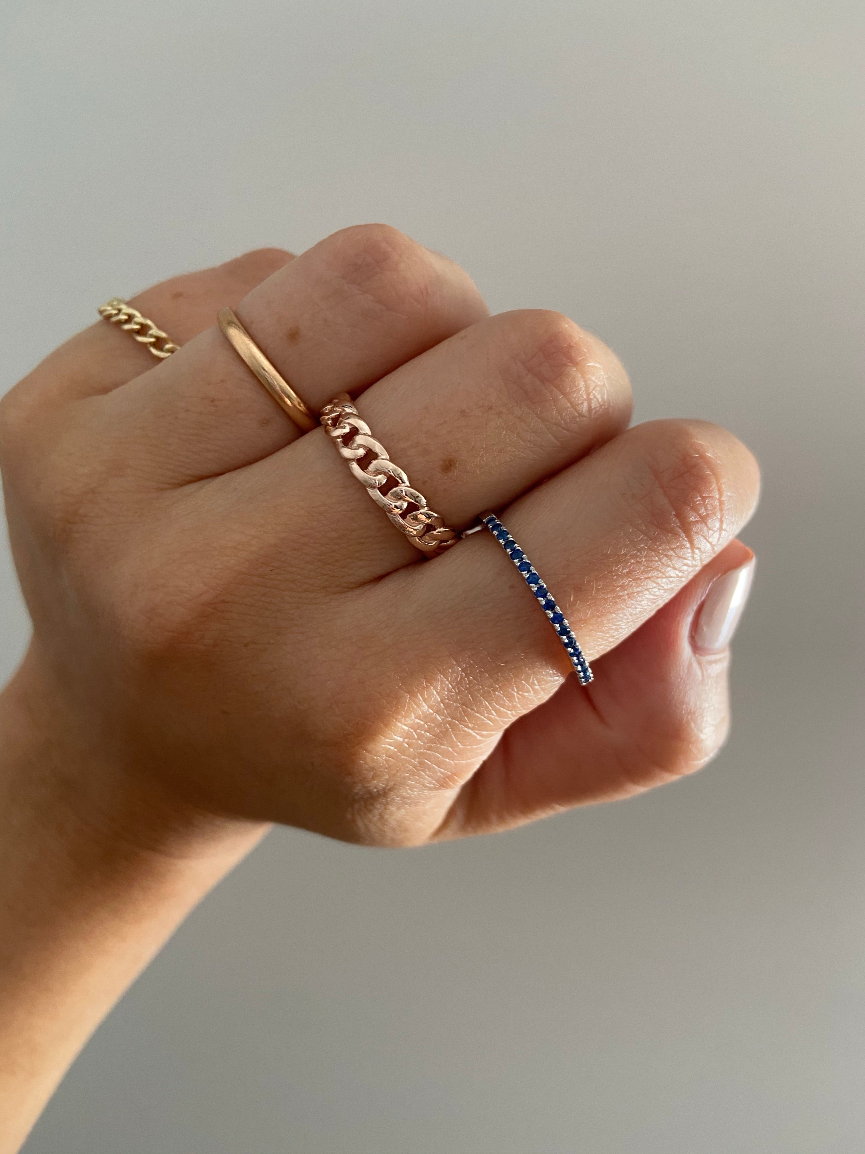 Detailed view of a 1.5mm Birthstone Ring on a person's finger, styled with various gold rings.