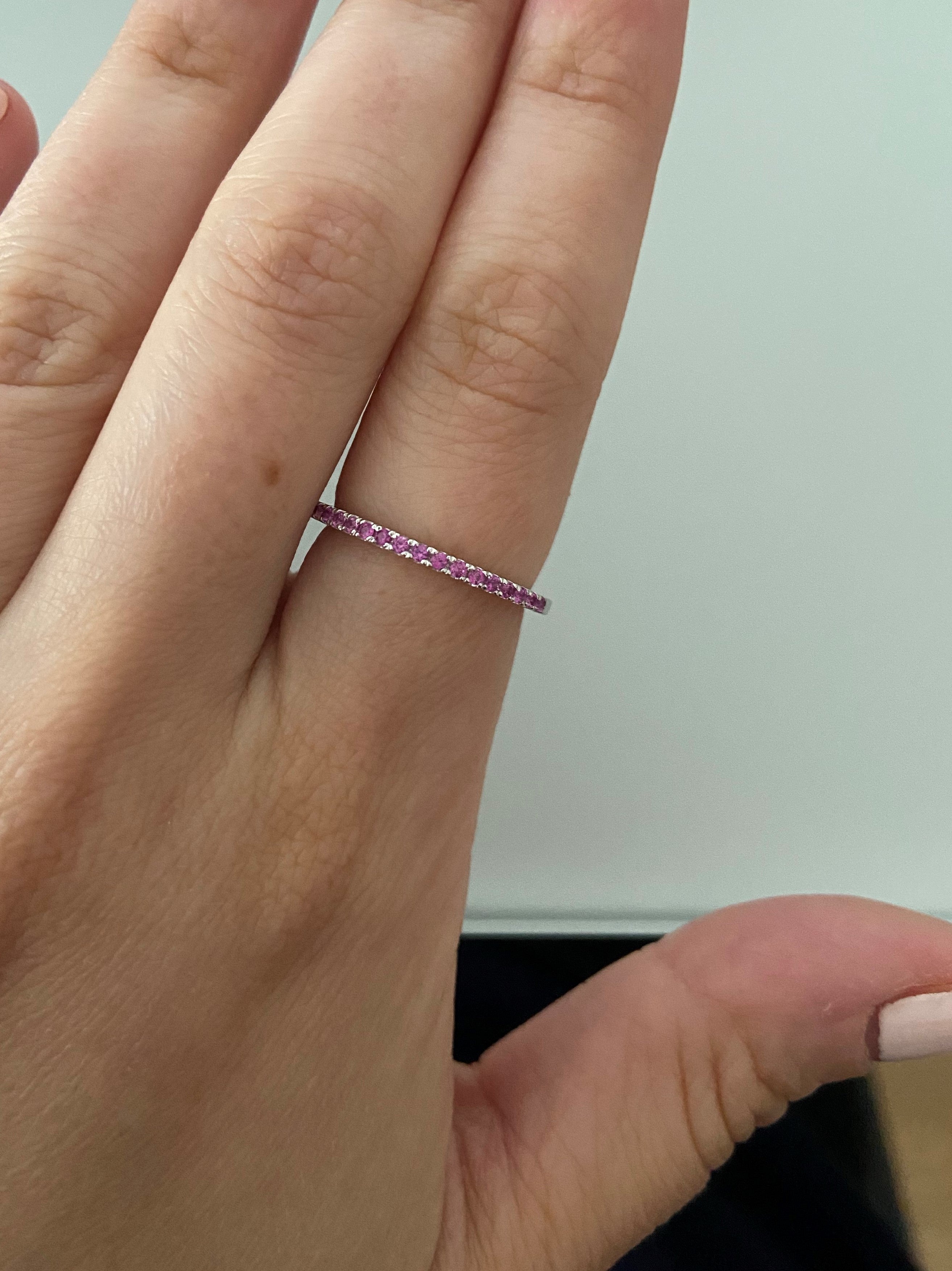 A close-up of a 1.5mm birthstone ring on a person's finger against a neutral background.