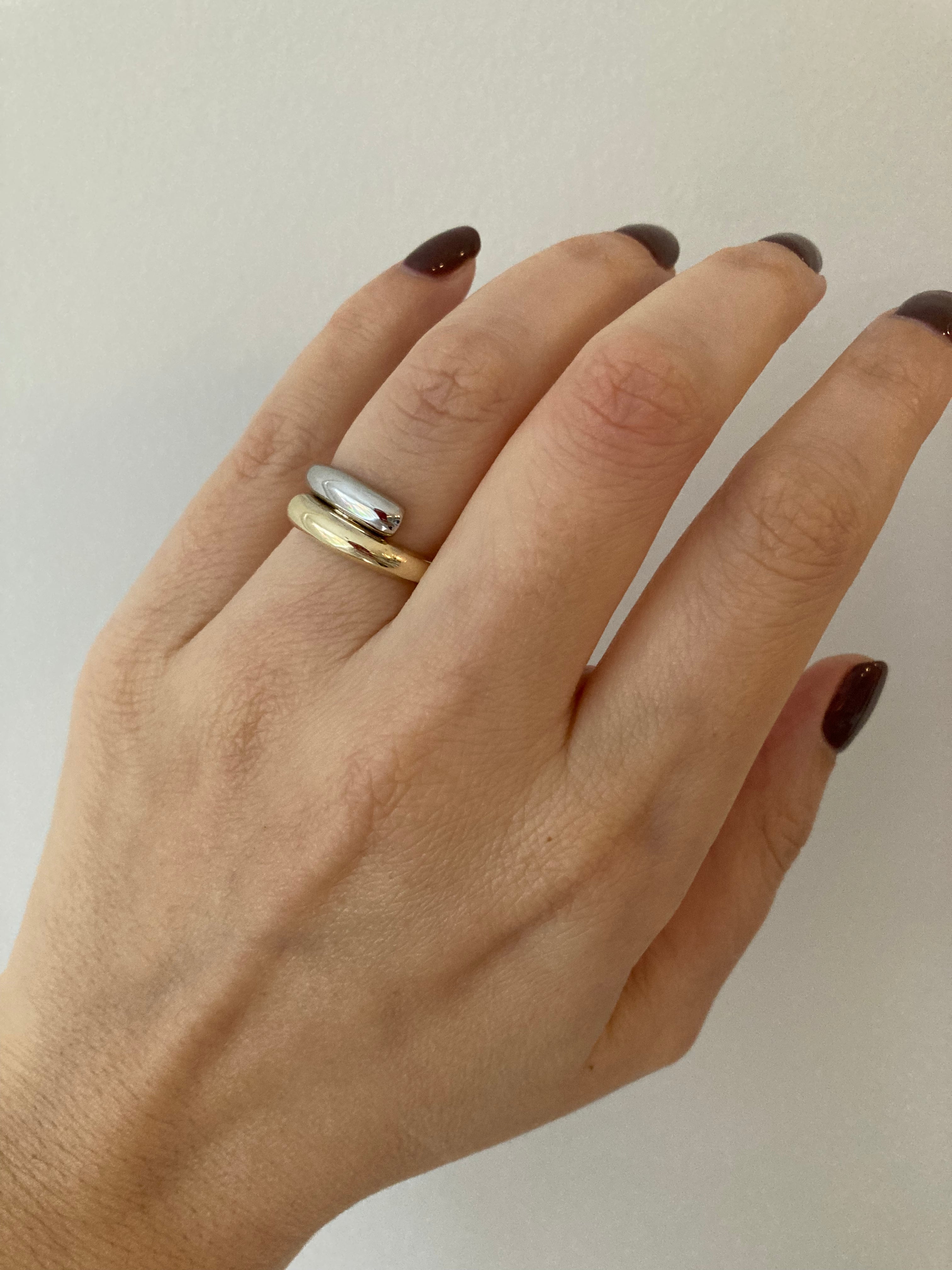 A chunky white and yellow gold wrap ring worn on a woman's hand against a neutral background.