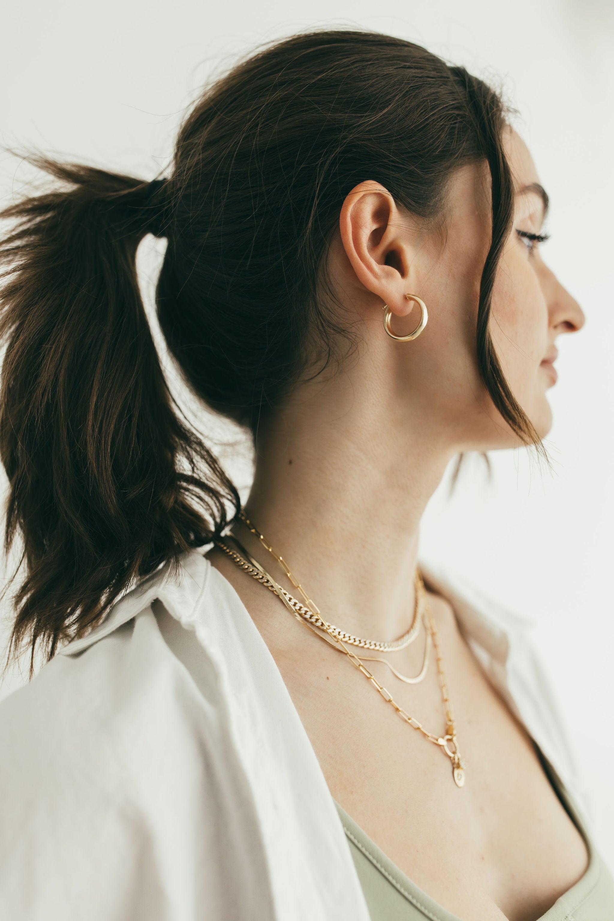 side profile of girl wearing gold necklaces and thick gold hoops
