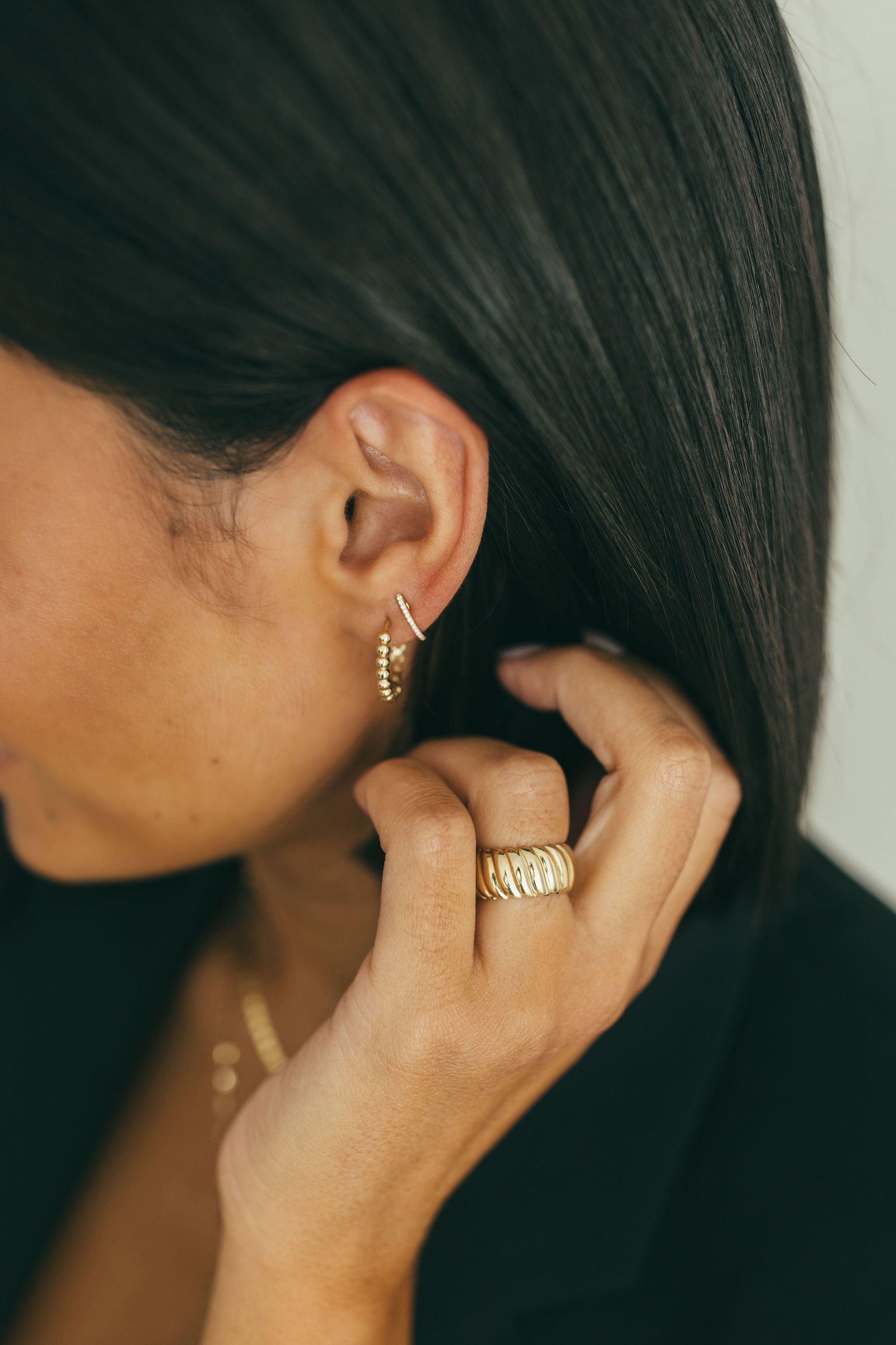 A woman wearing yellow gold earrings and a yellow gold chunky wide croissant ring.
