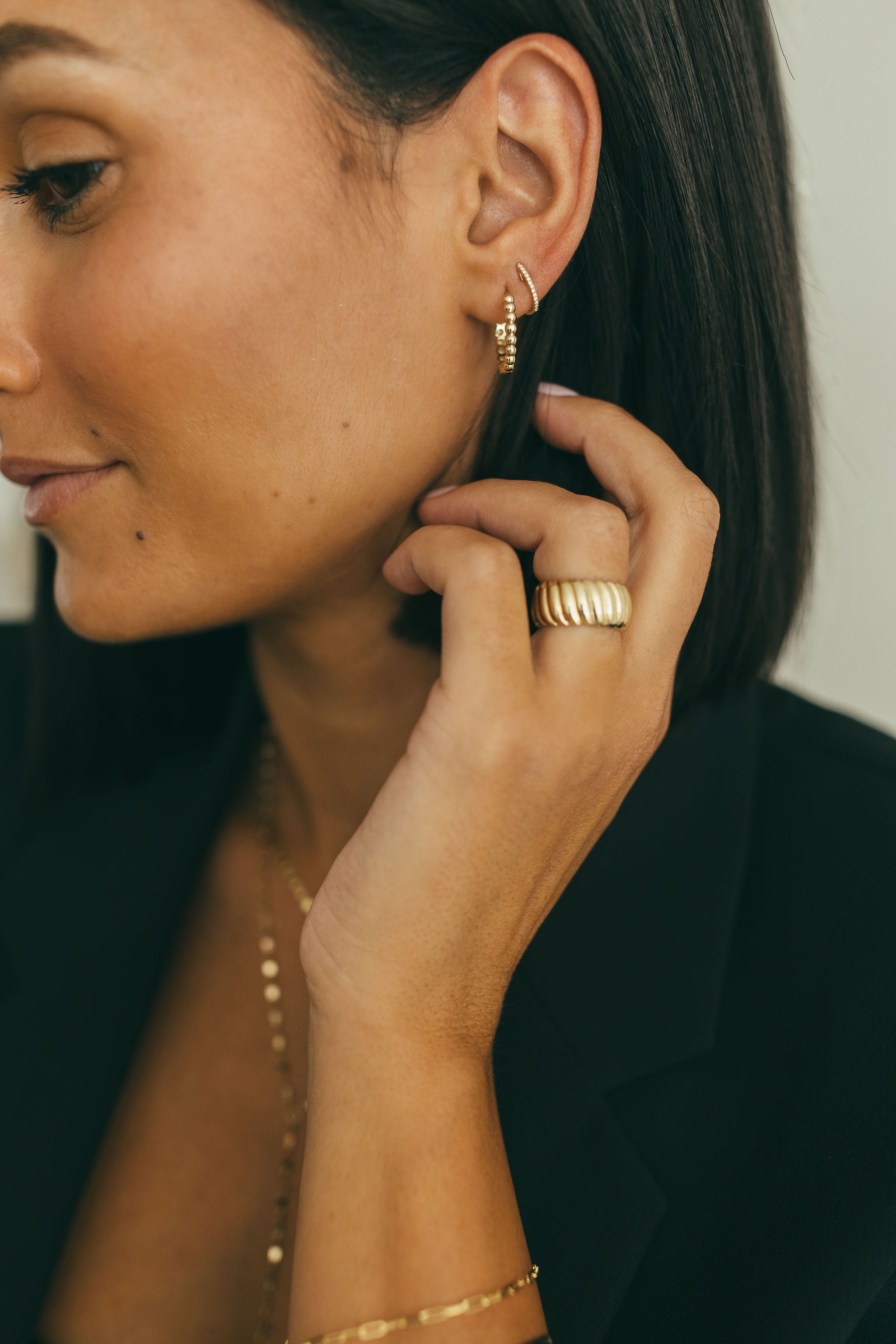 A woman wearing yellow gold earrings and a yellow gold chunky wide croissant ring.