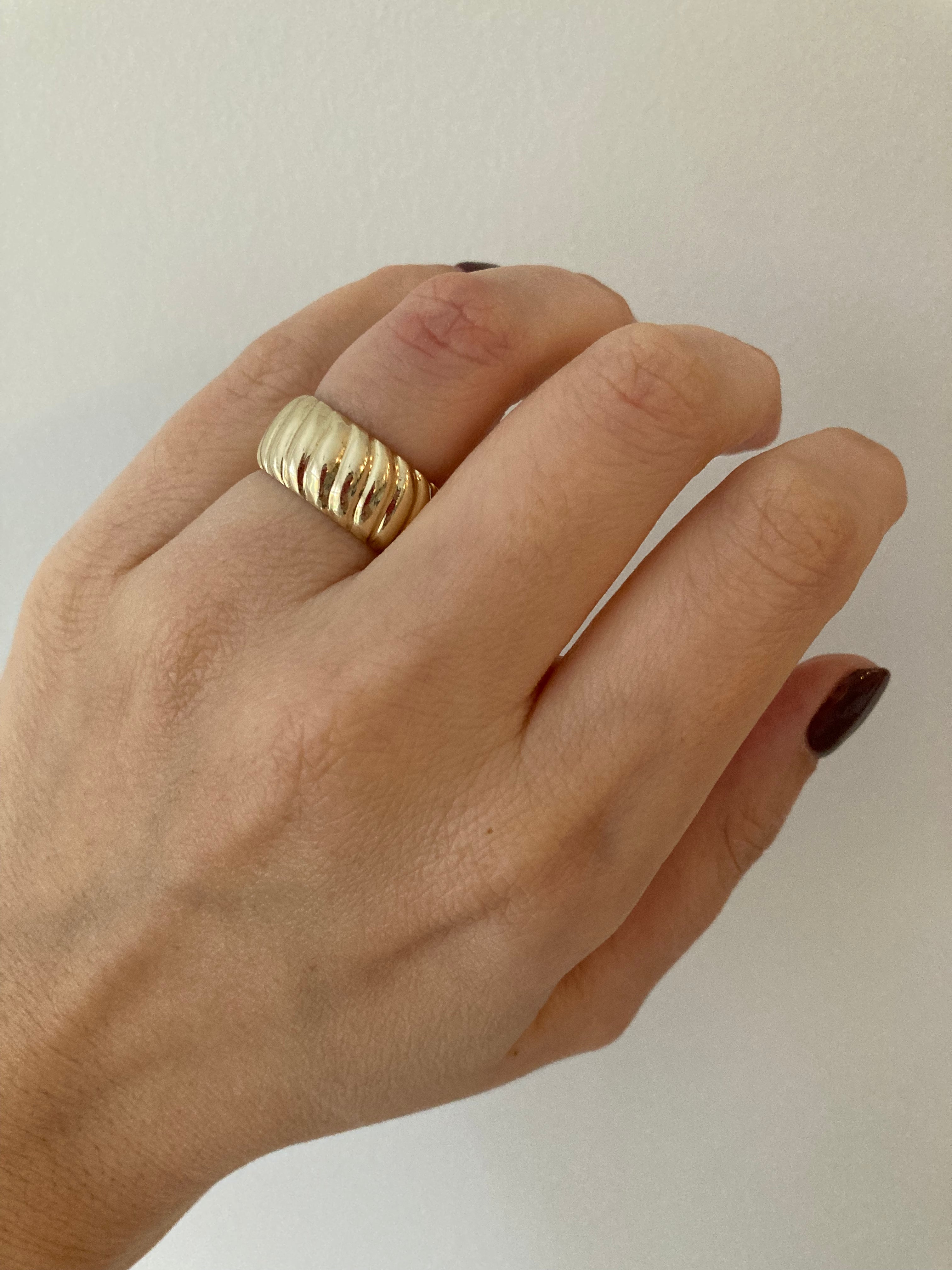 A yellow gold chunky wide croissant ring worn on a person's finger against a neutral background.