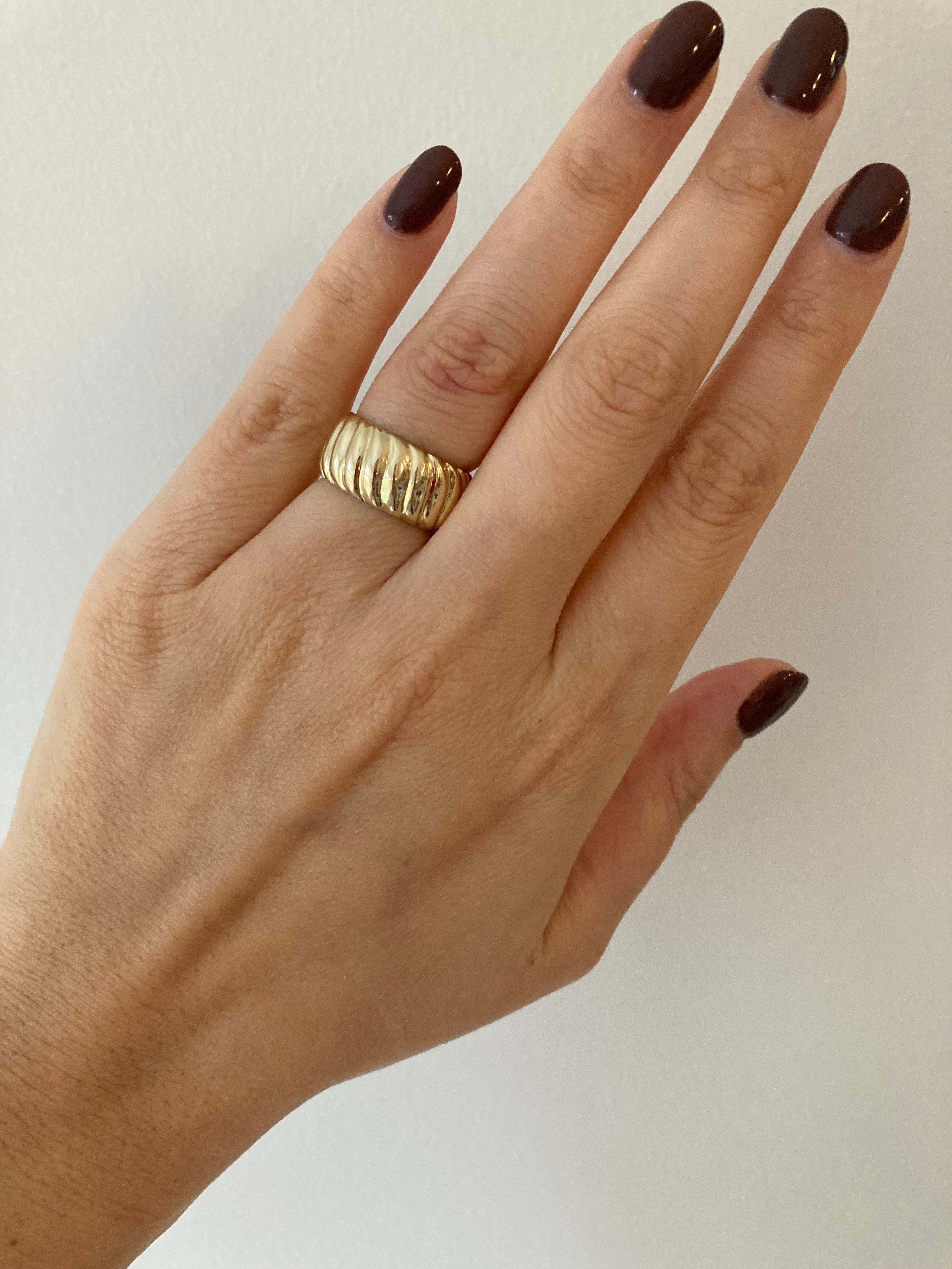 A yellow gold chunky wide croissant ring worn on a person's finger against a neutral background.