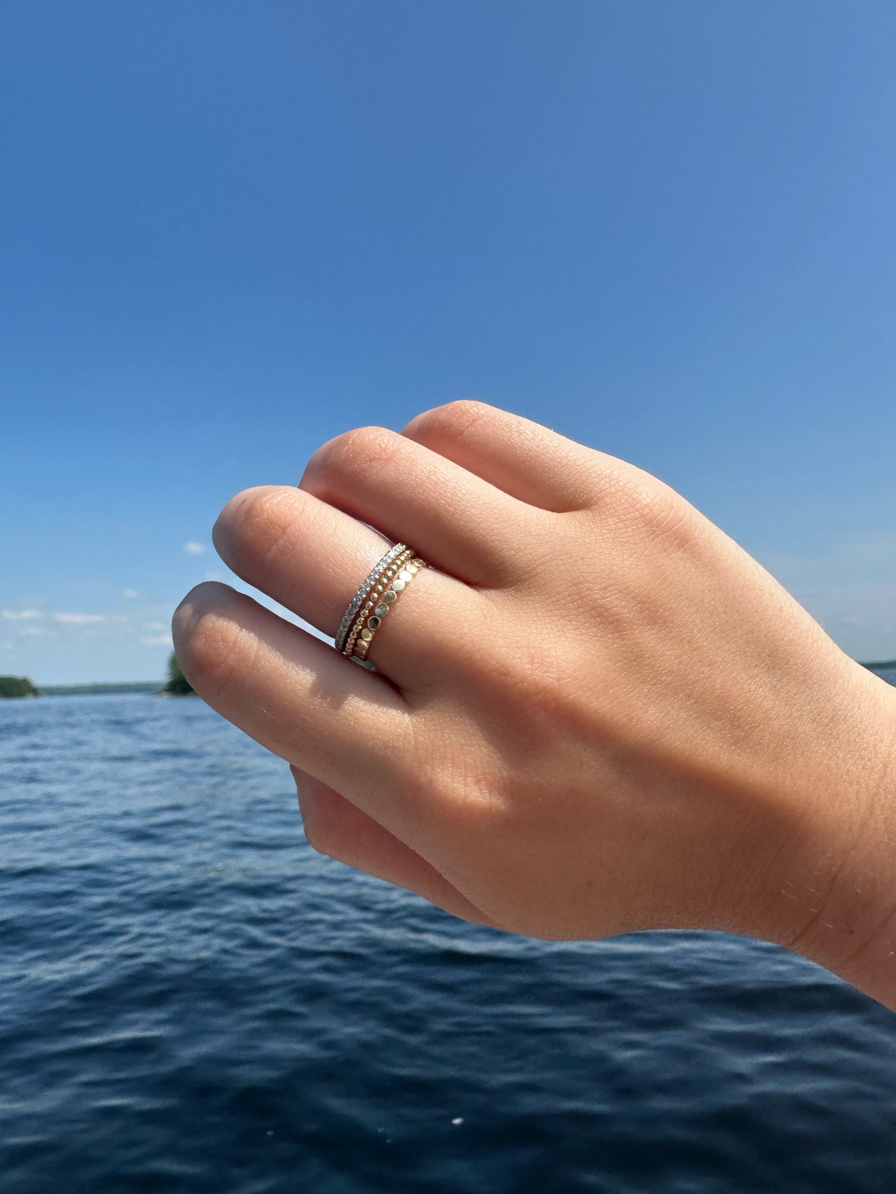 A stack of three gold rings on a person's hand with water in the background.