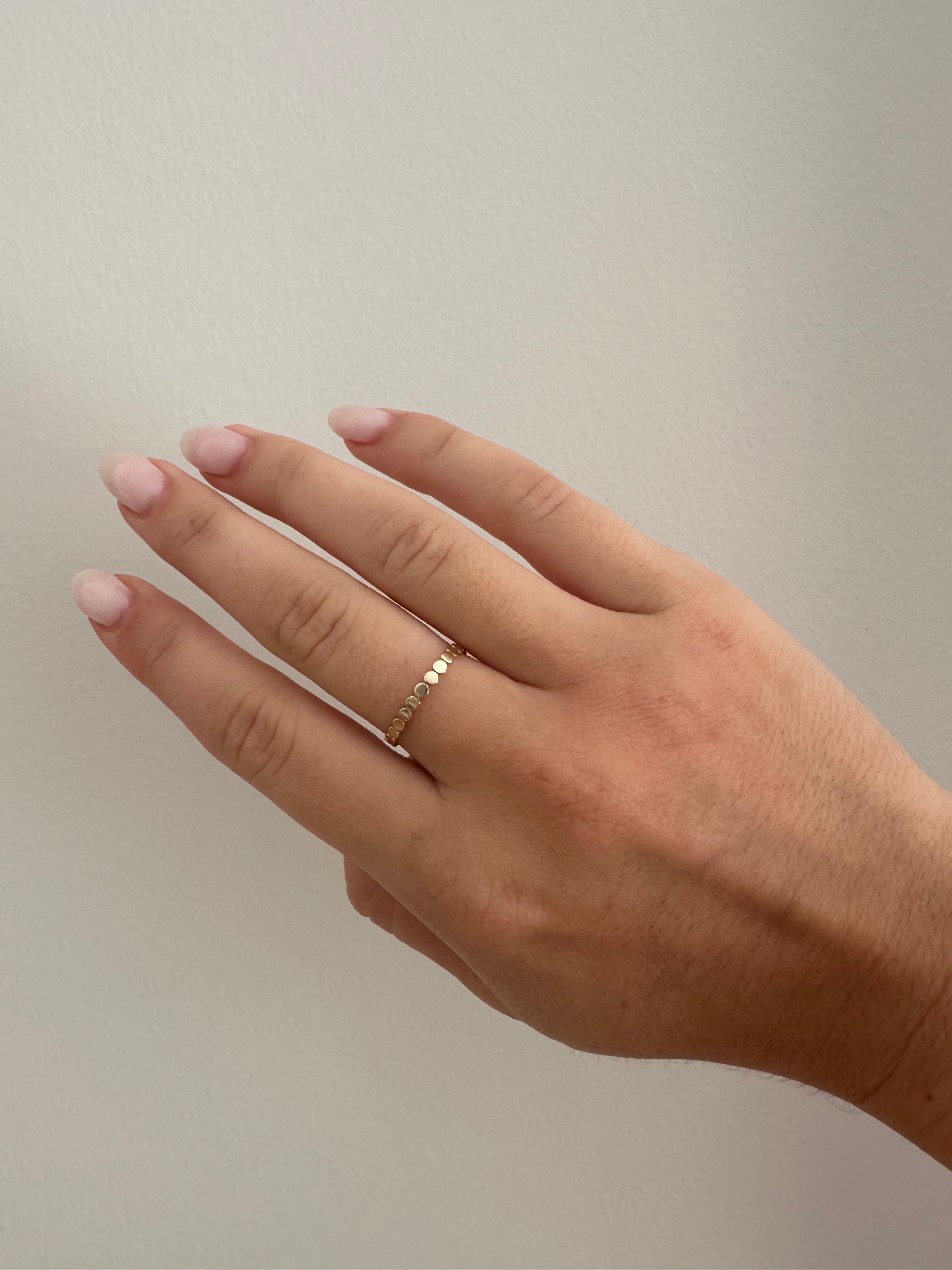 A gold dotted ring on a person's finger against a neutral background.