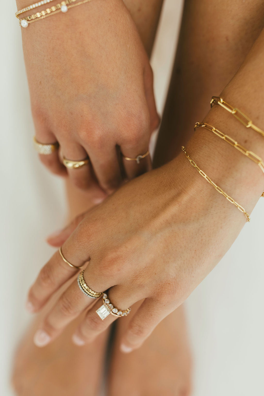 Close-up of hands wearing gold jewellery including gold rings and bracelets on a white background.