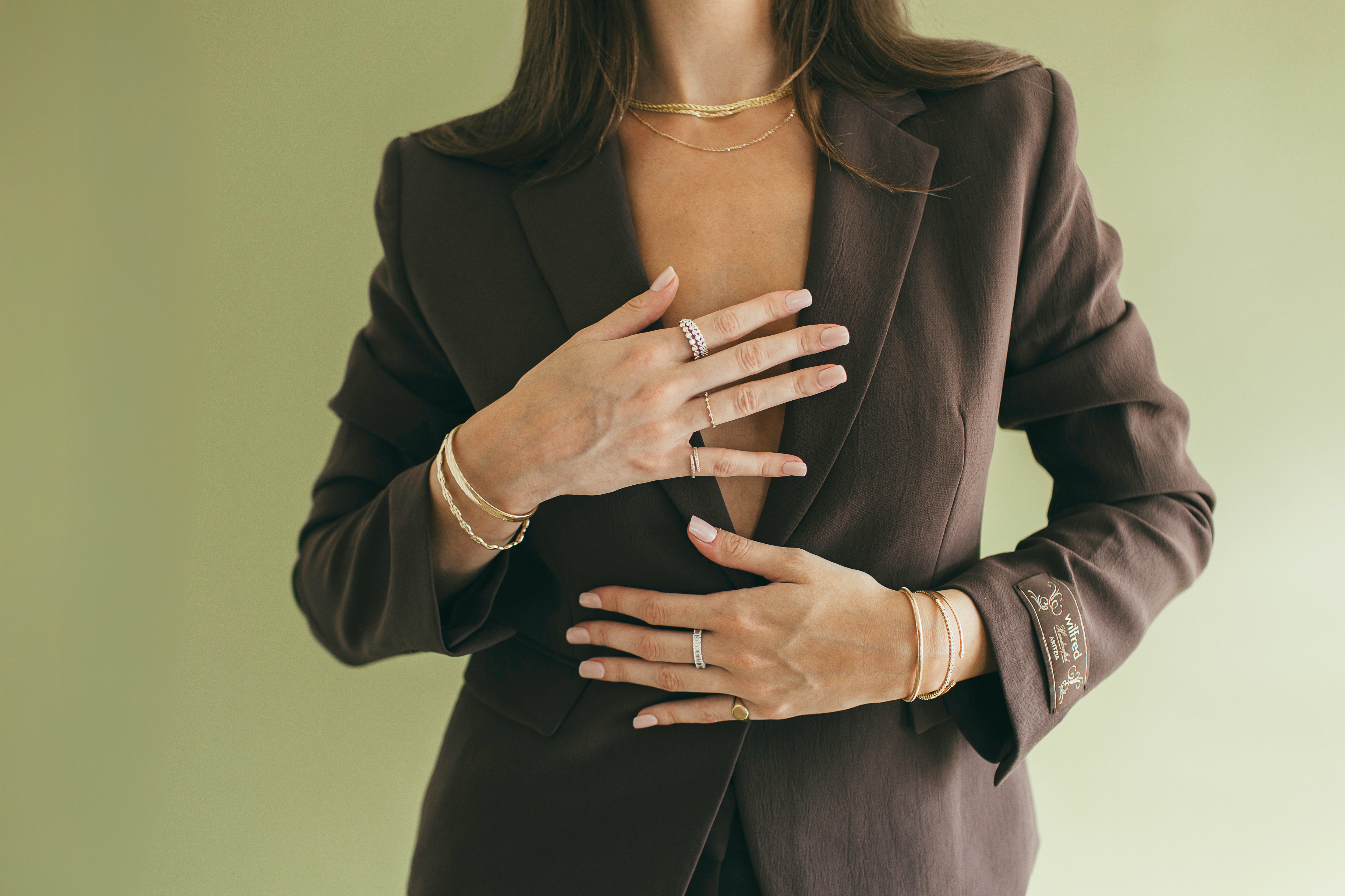 Person wearing a dark suit with gold jewelry on a plain background.