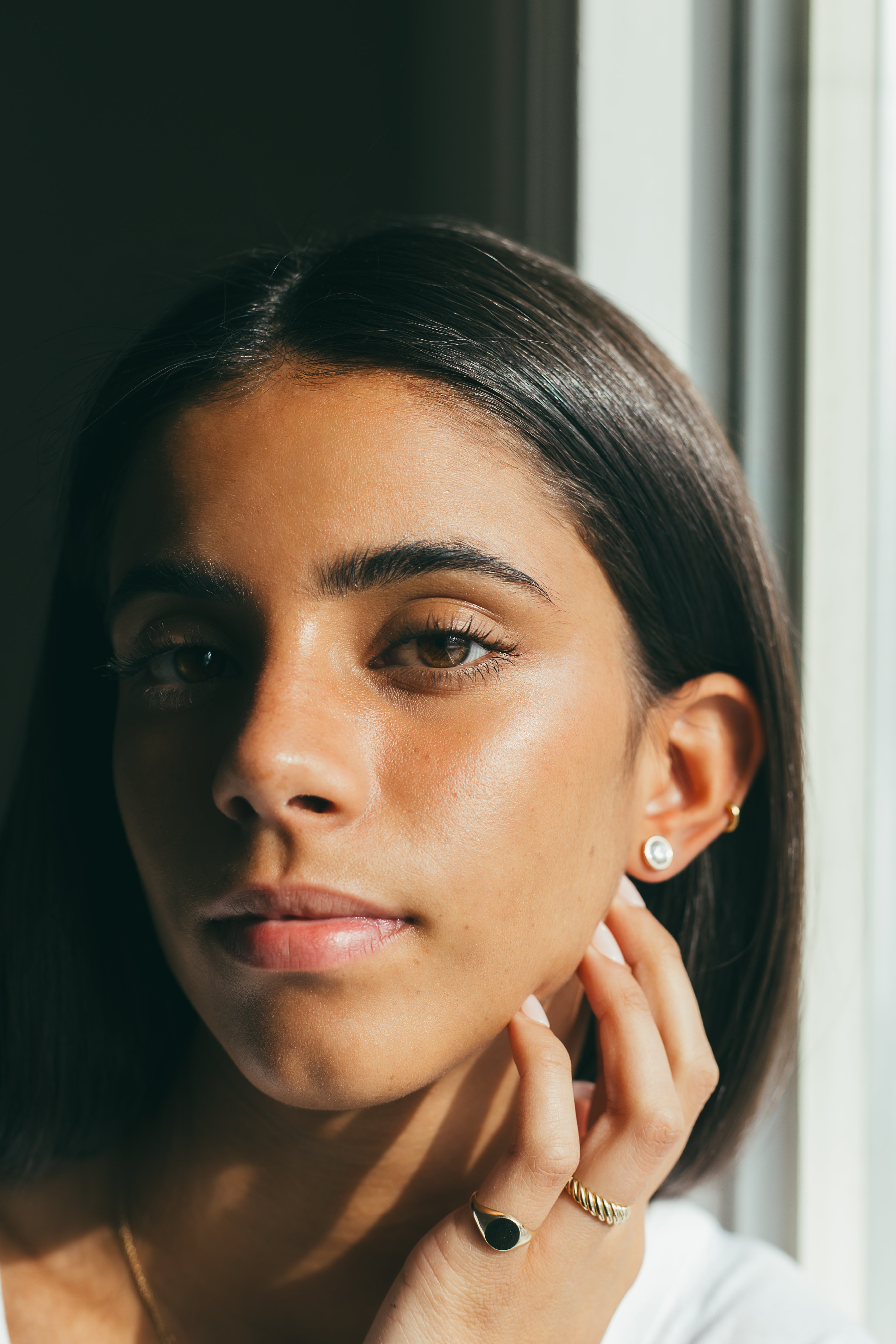 Woman styled with earrings and gold rings, looking at the camera.