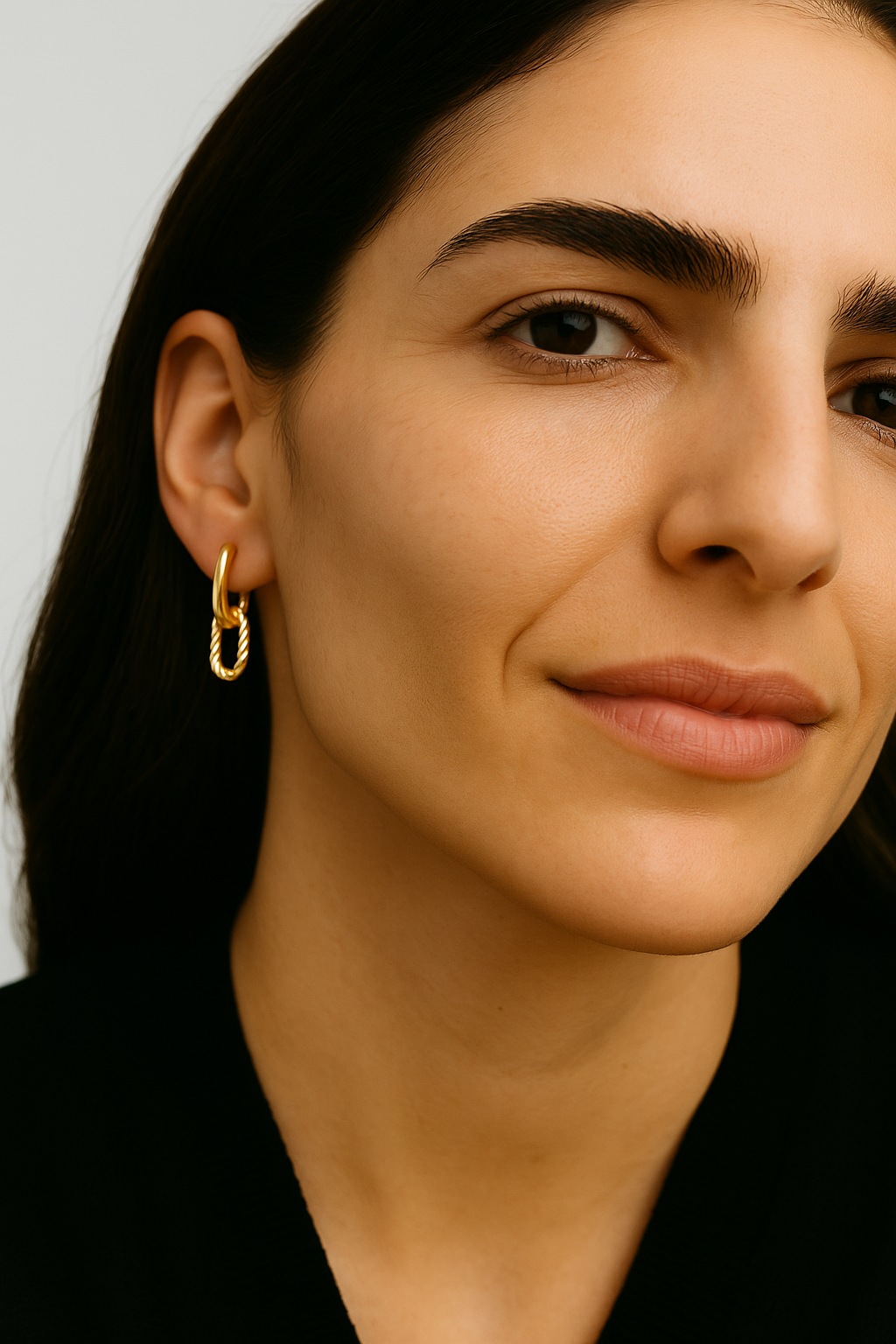 Close-up of a woman wearing a gold hoop earring against a neutral background