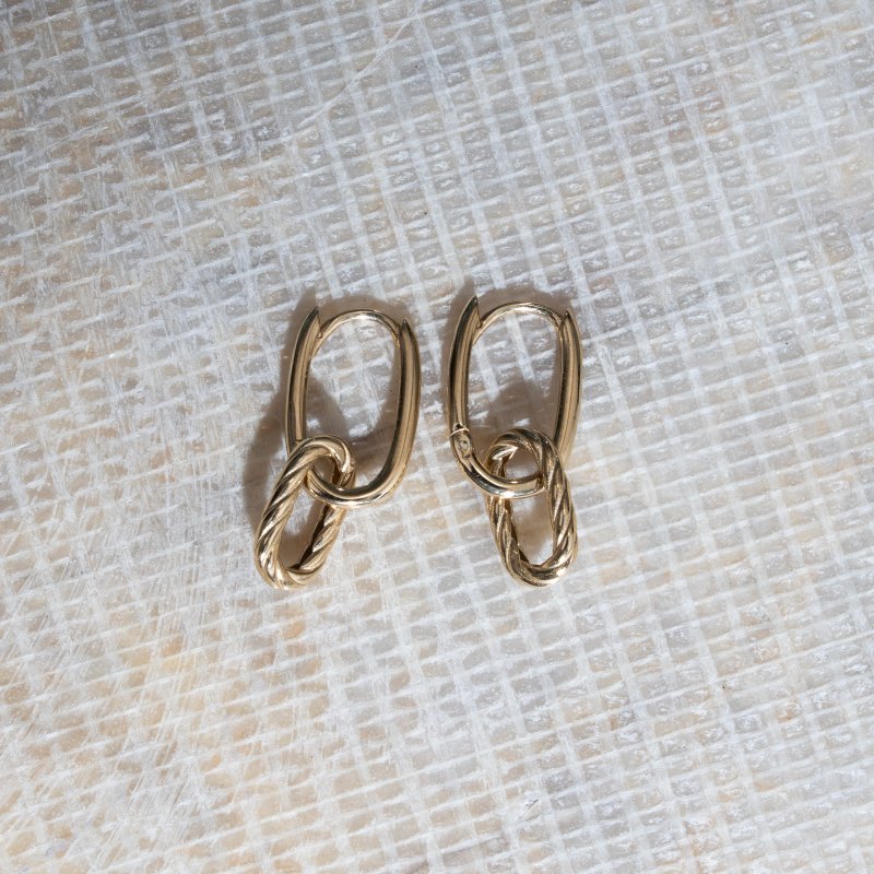 Pair of gold chain earrings on a textured beige surface