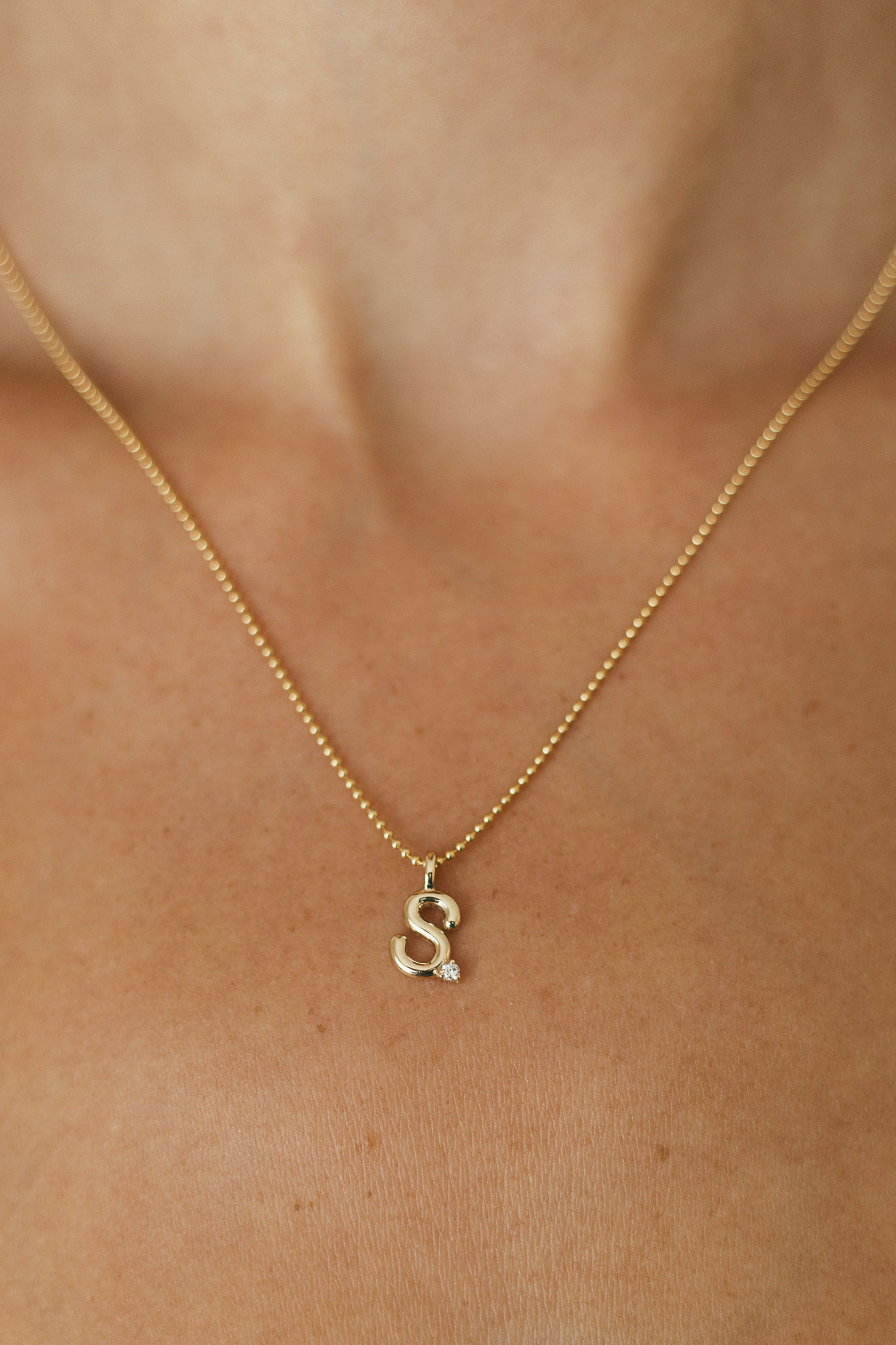 Gold necklace with a small initial pendant on a person's neck