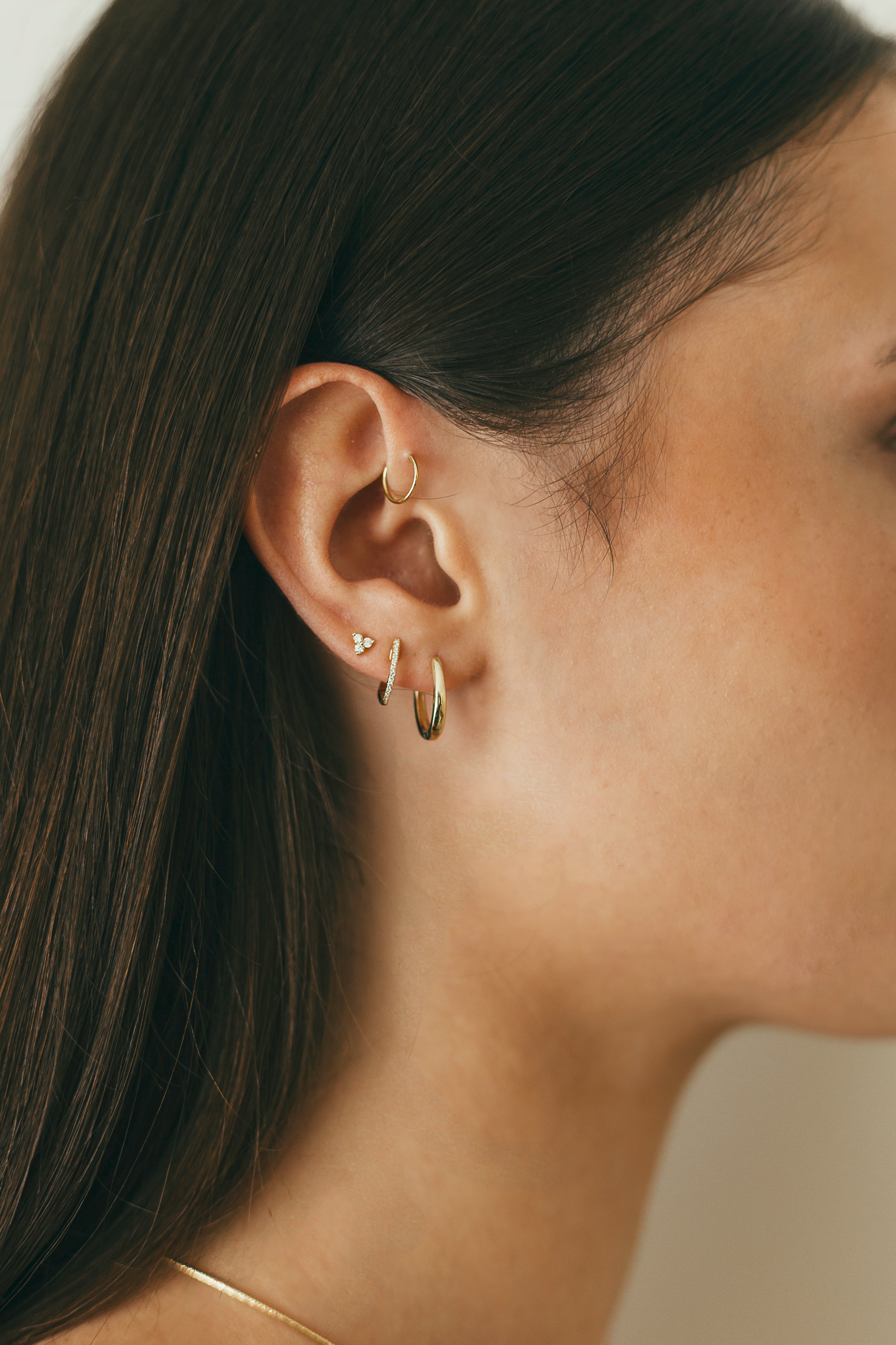 Close-up of a person wearing gold hoop earrings with a neutral background