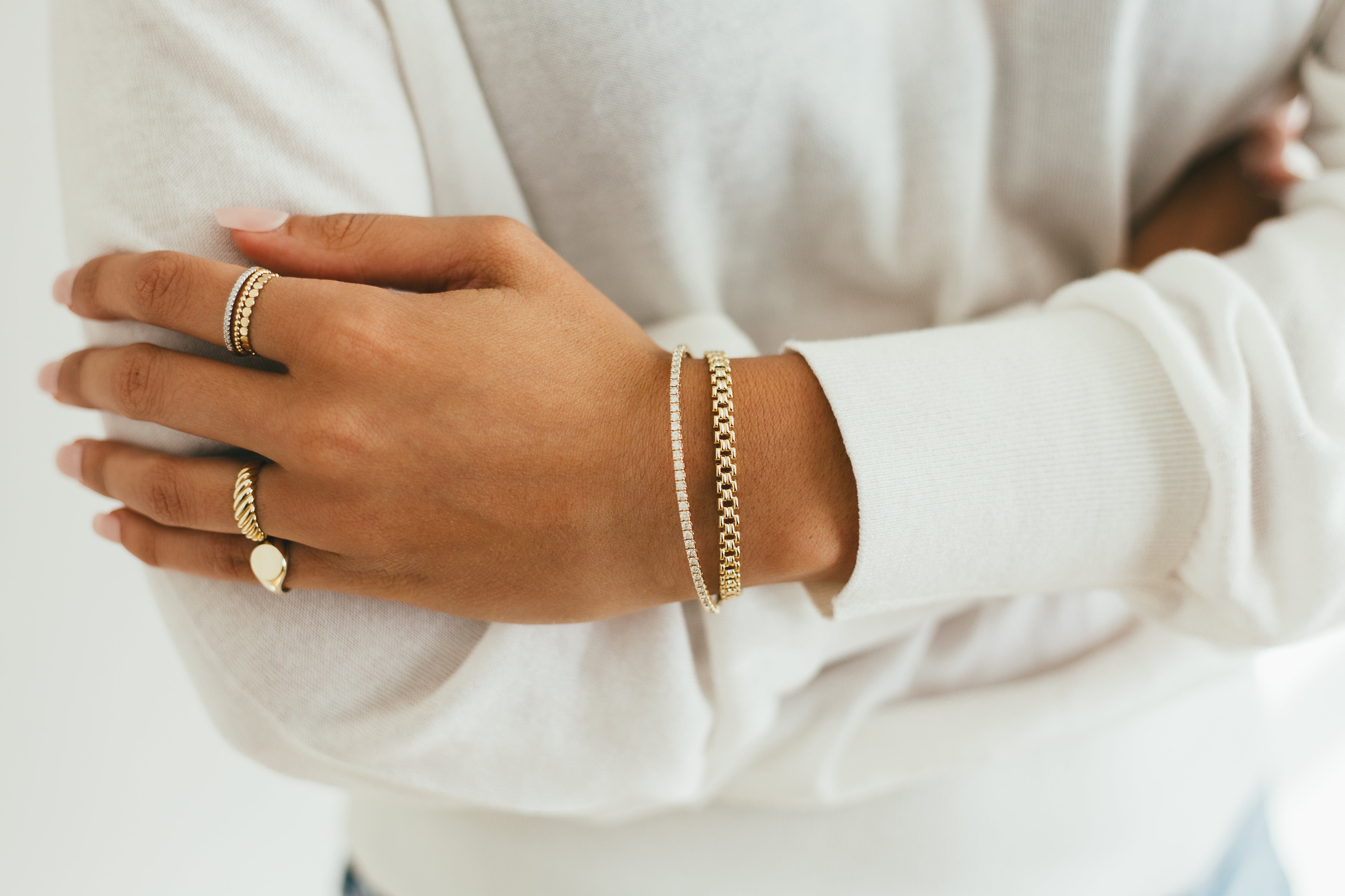 Close-up of a hand wearing gold rings and bracelets on a neutral background.
