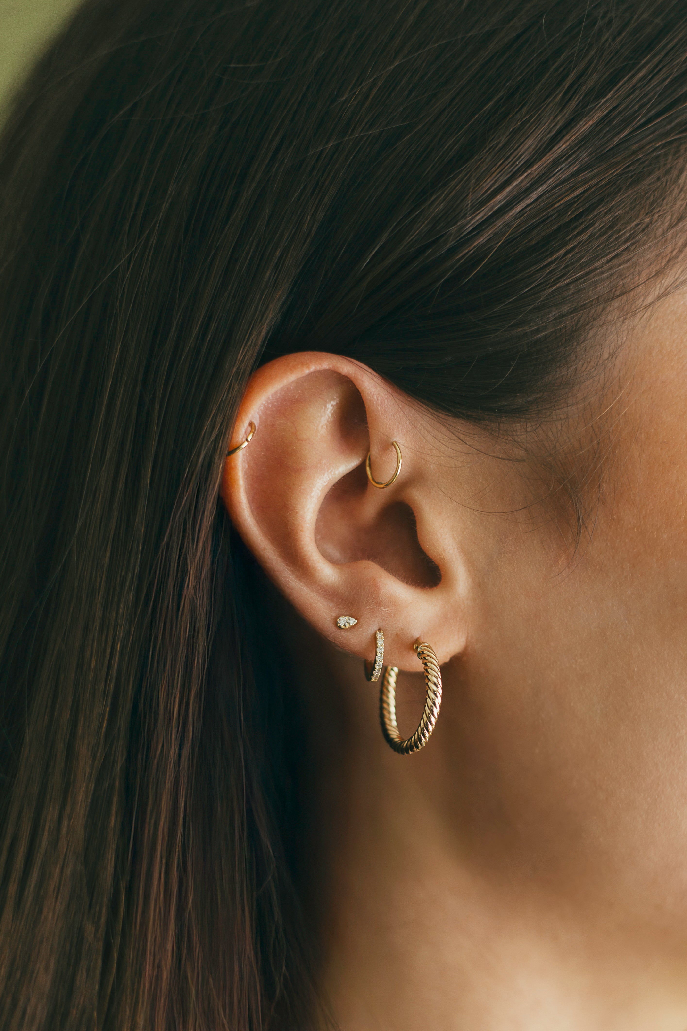 Close-up of an ear with gold twisted hoop earrings and a small stud.