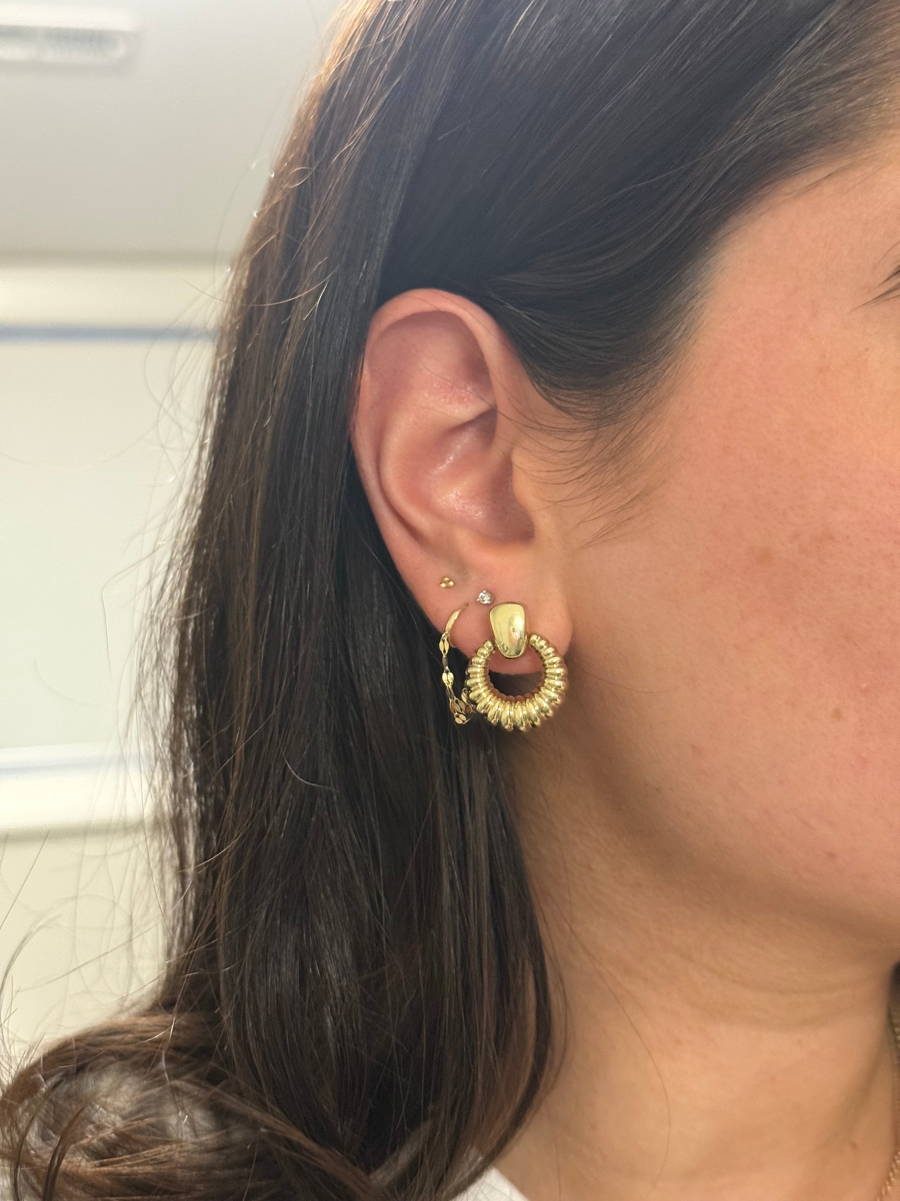 Close-up of an ear wearing a gold earring with a blurred background