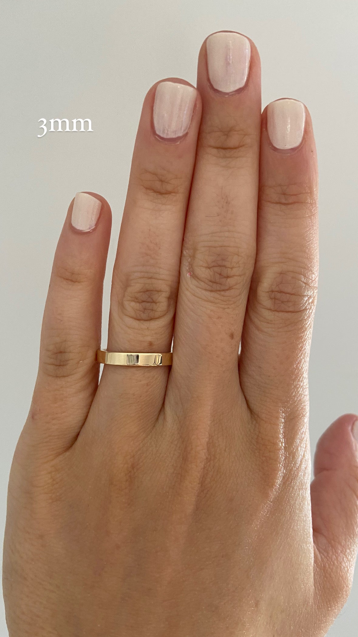 A close up of a person's hand, wearing a gold wide flat cigar band on their index finger, with text indicating a ring width of "3mm".