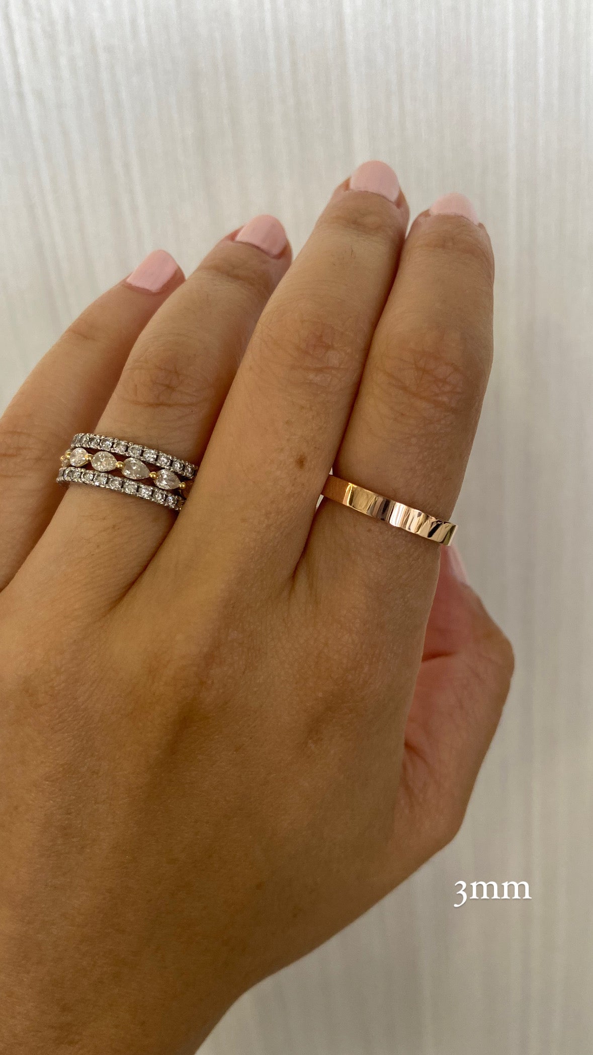 A close up of a person's hand wearing a single gold wide flat cigar band on their pointer finger, and a stack of gold and diamond rings on their index finger, with text indicating a "3mm" ring width.