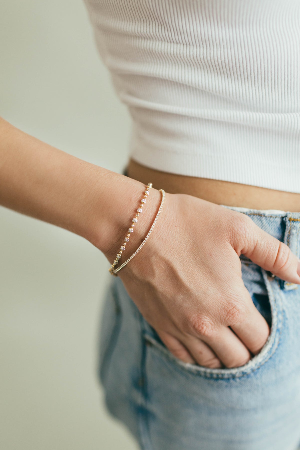 Person wearing a white and yellow gold bead bracelet, stacked with a diamond tennis bracelet. 