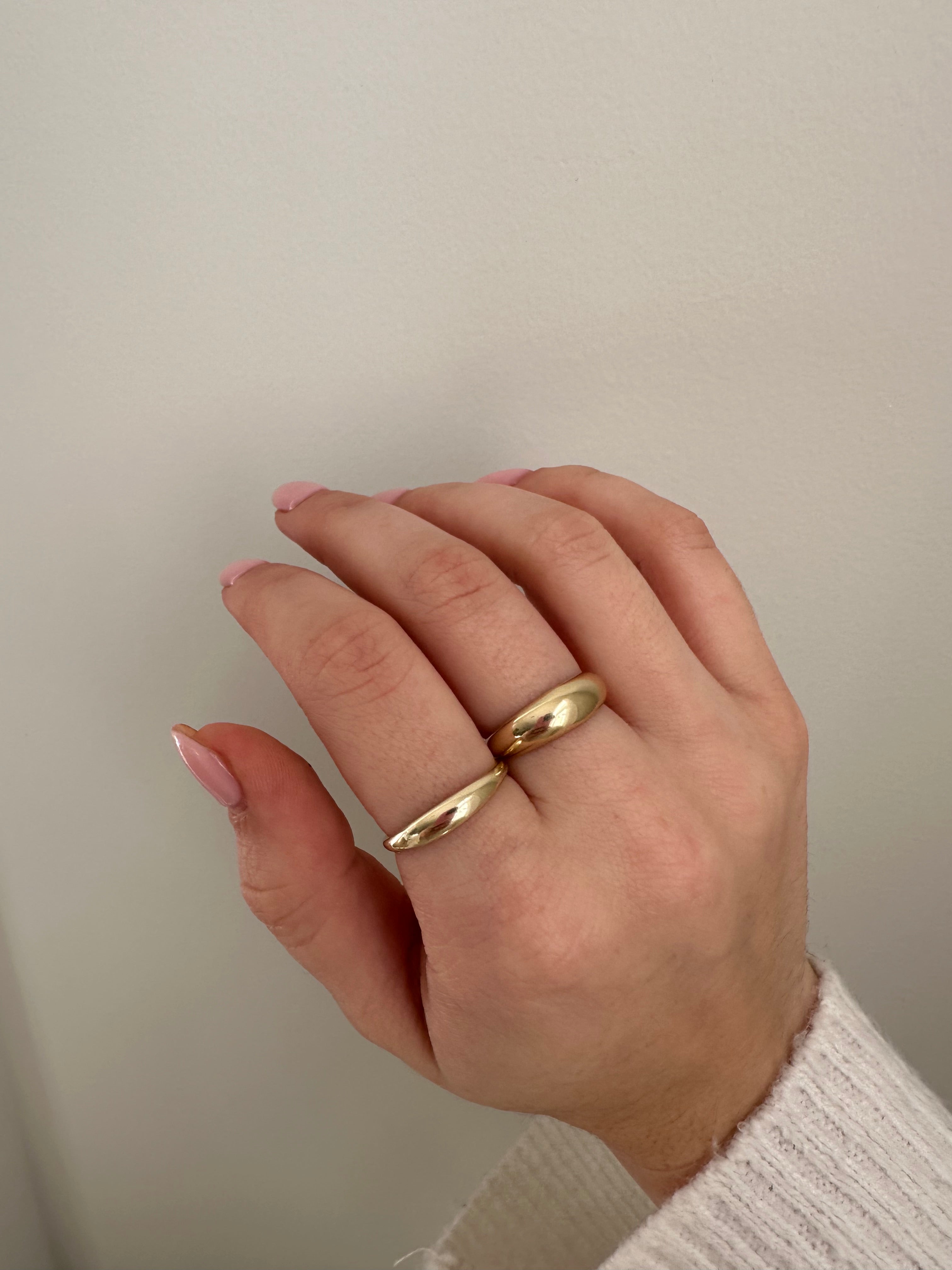 A close-up of a person's hand wearing a gold large dome ring and a gold mini dome ring.