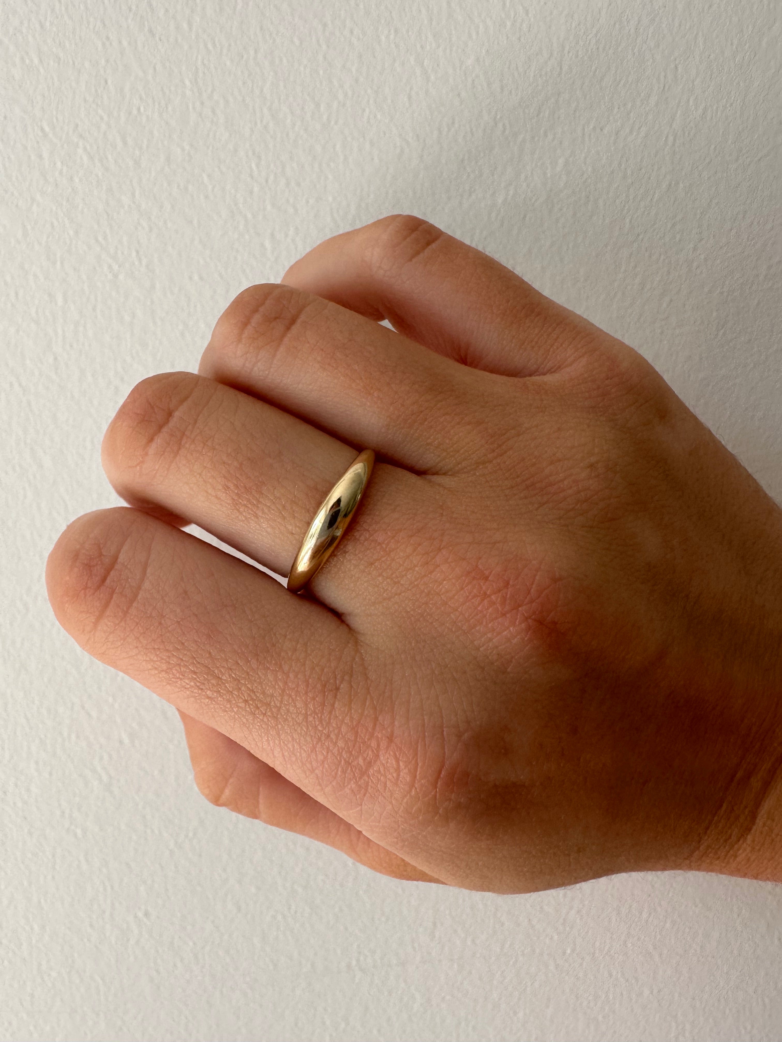 A close-up of a gold mini dome ring worn on a person's finger.