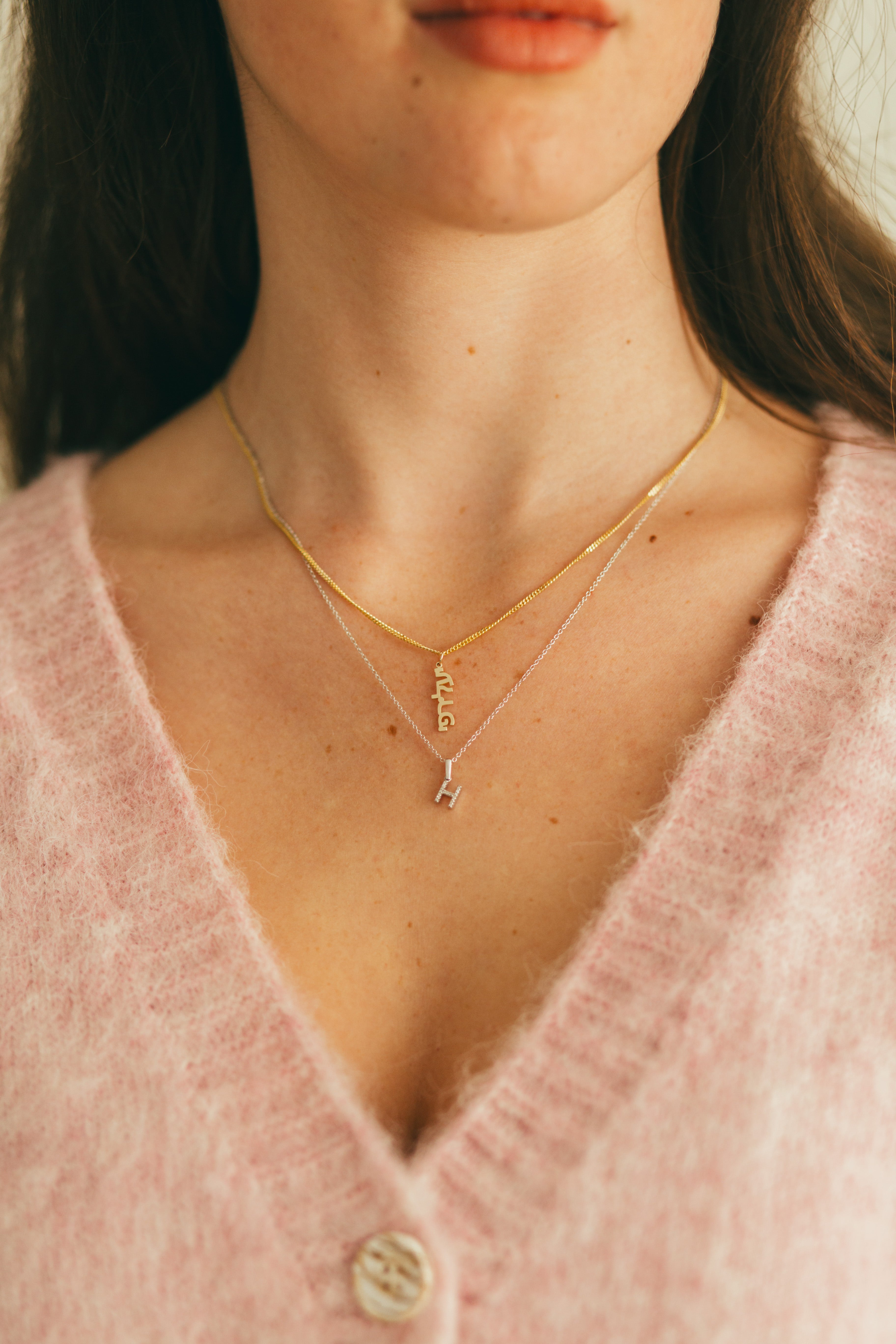 a girl wearing a hebrew charm necklace and a diamond initial charm necklace 