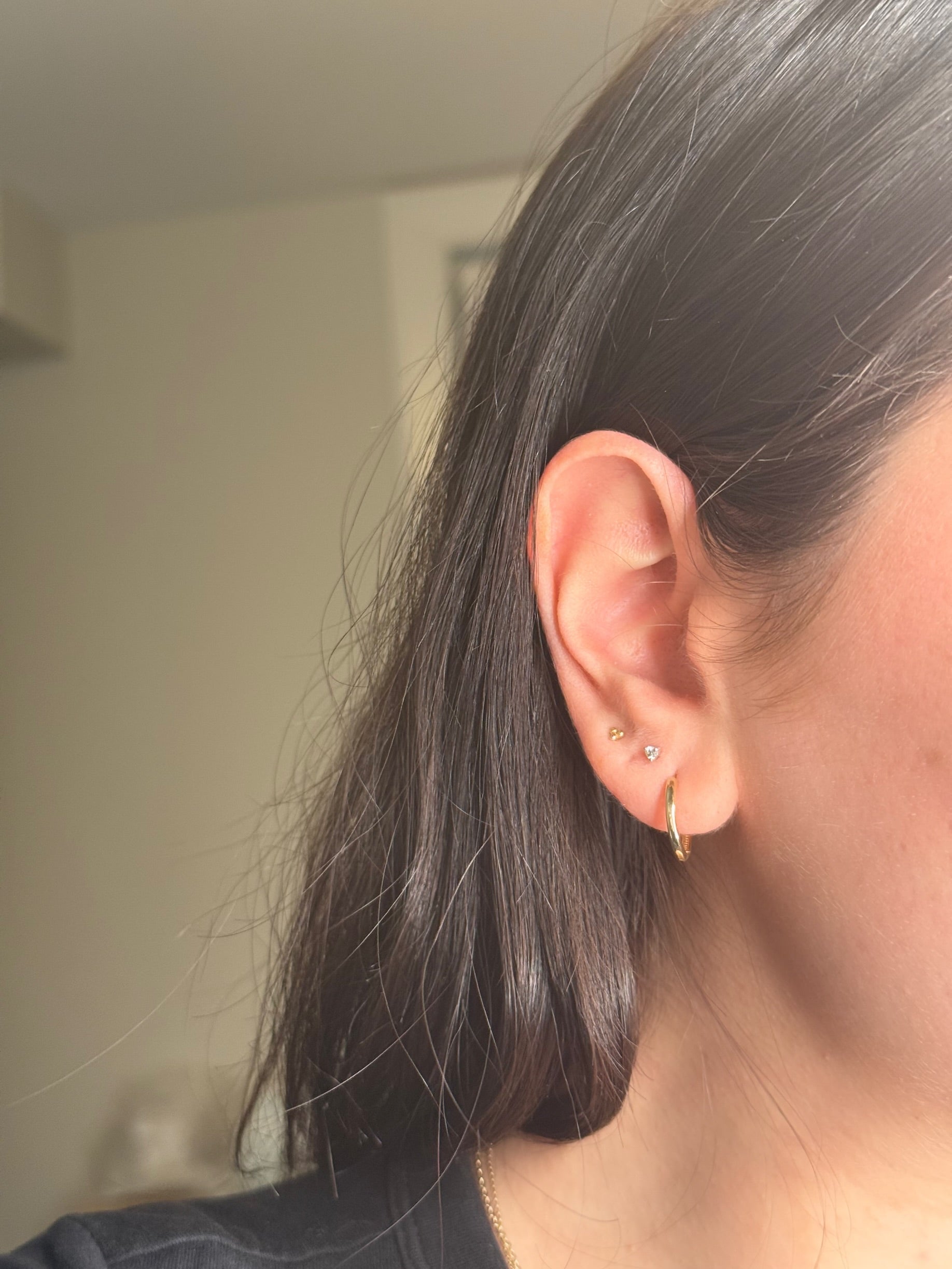 Close-up of a simple gold huggie hoop on the ear. 