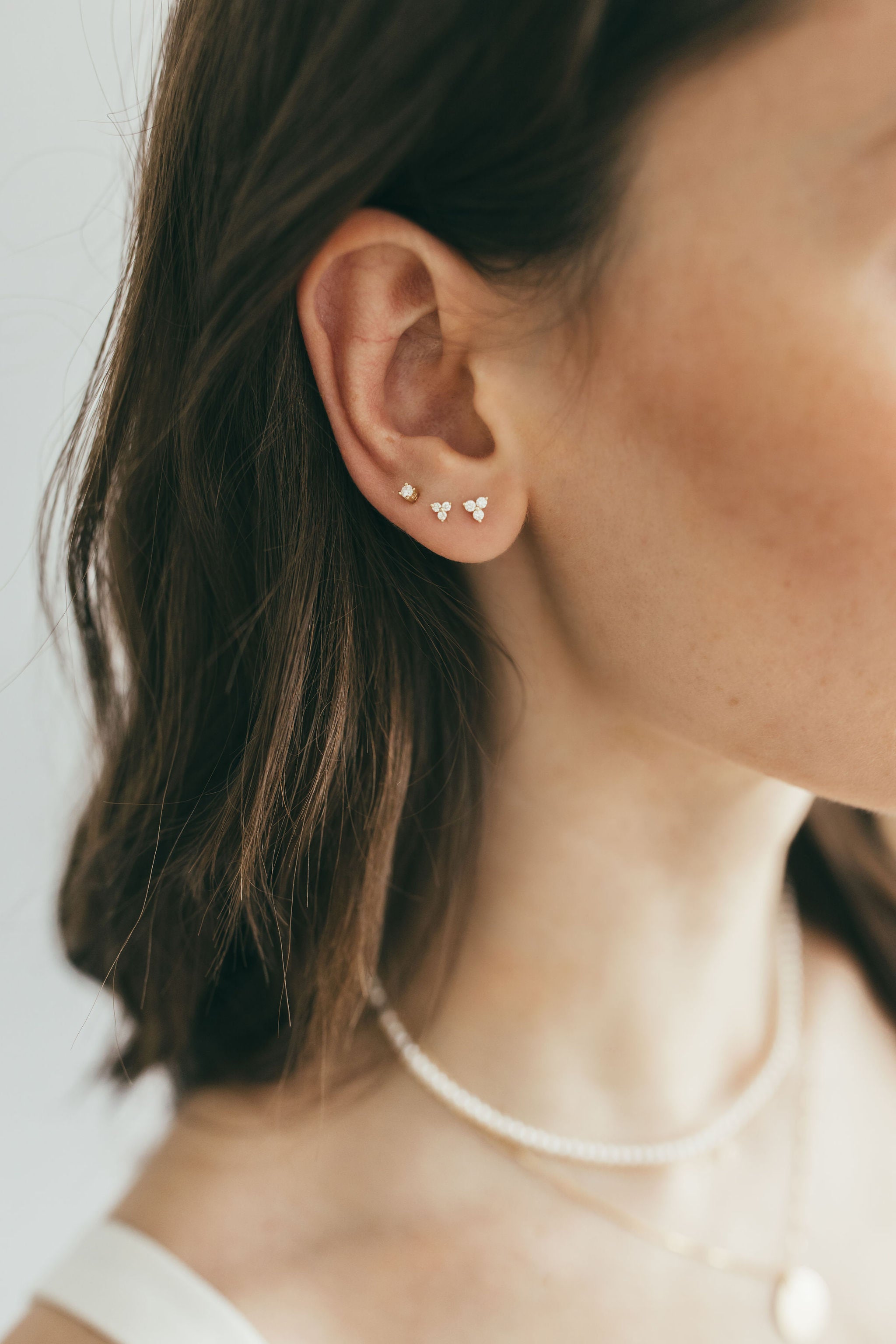 close up of ear stack including two sizes of gold and diamond trio studs and a diamond stud