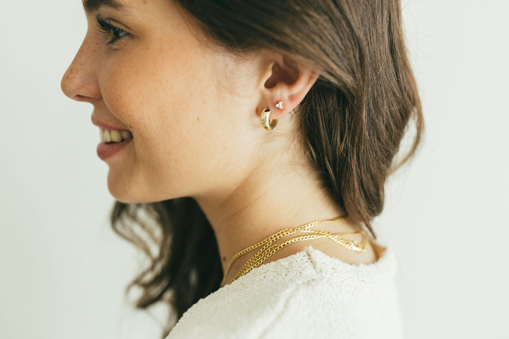 Woman wearing gold and diamomnd earrings and necklace against a white background
