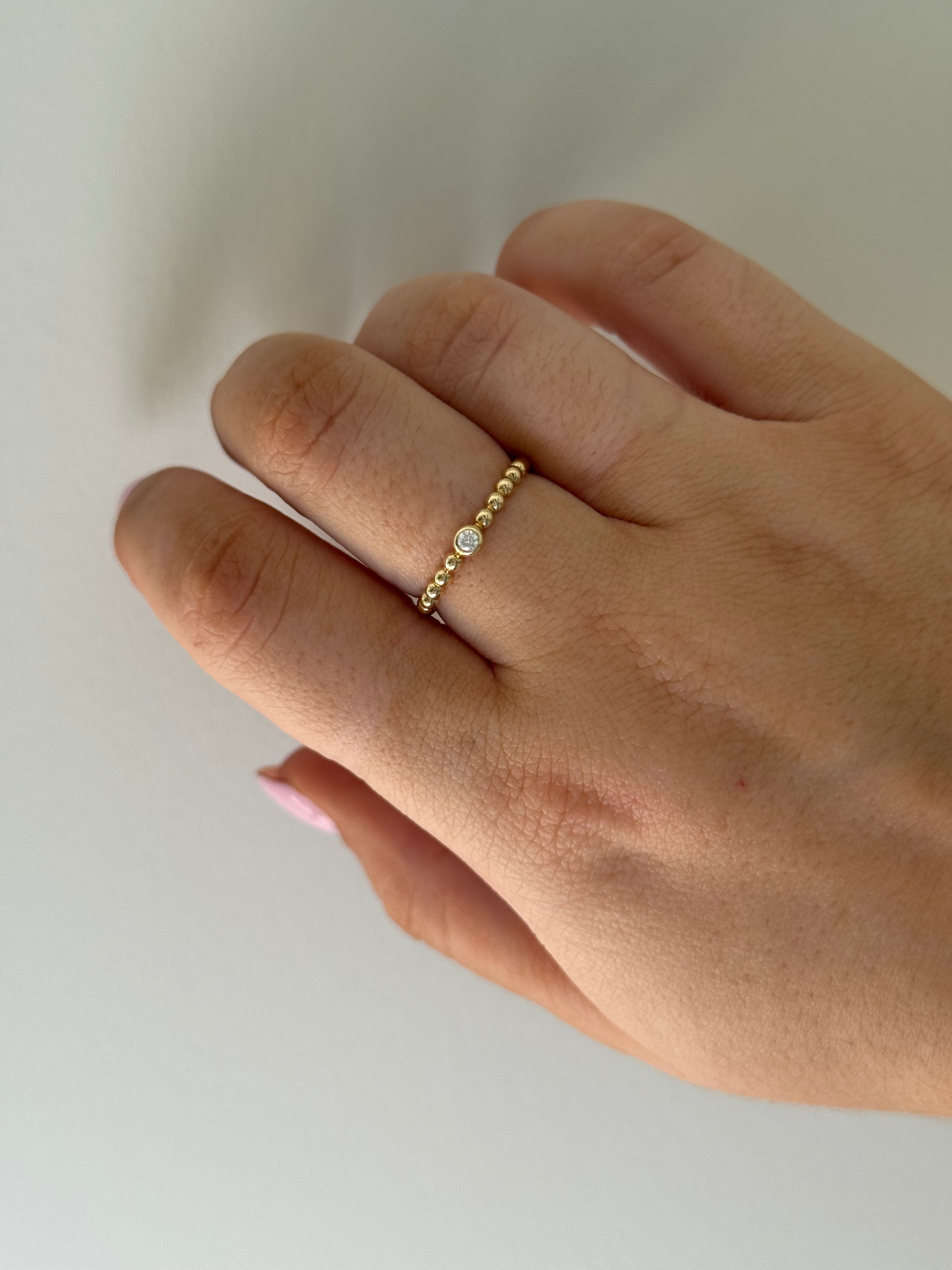 Gold bead ring with a single diamond on a person's finger against a neutral background.