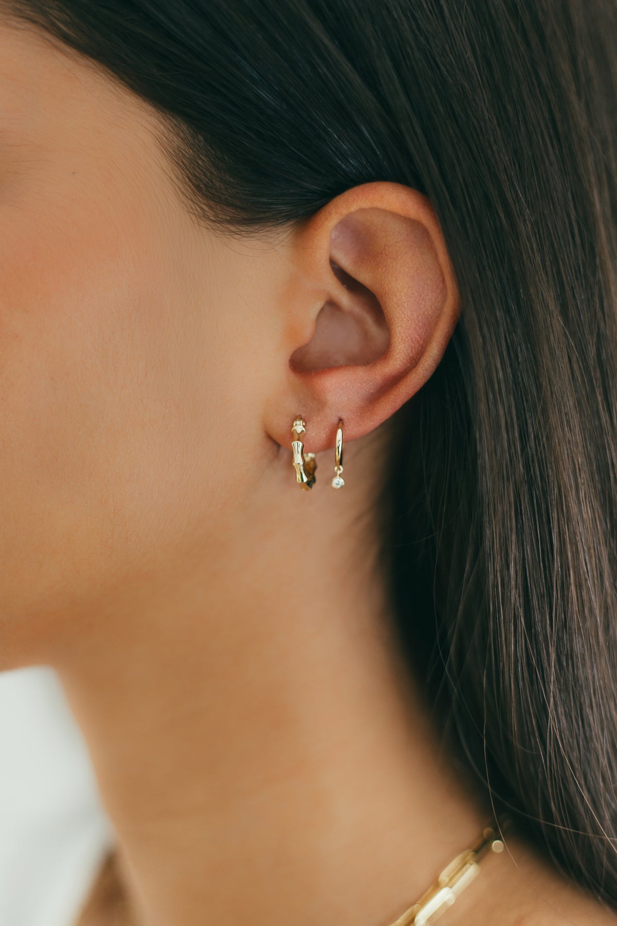 Close-up of an ear wearing gold hoop earrings and dangling diamond huggies with a blurred background