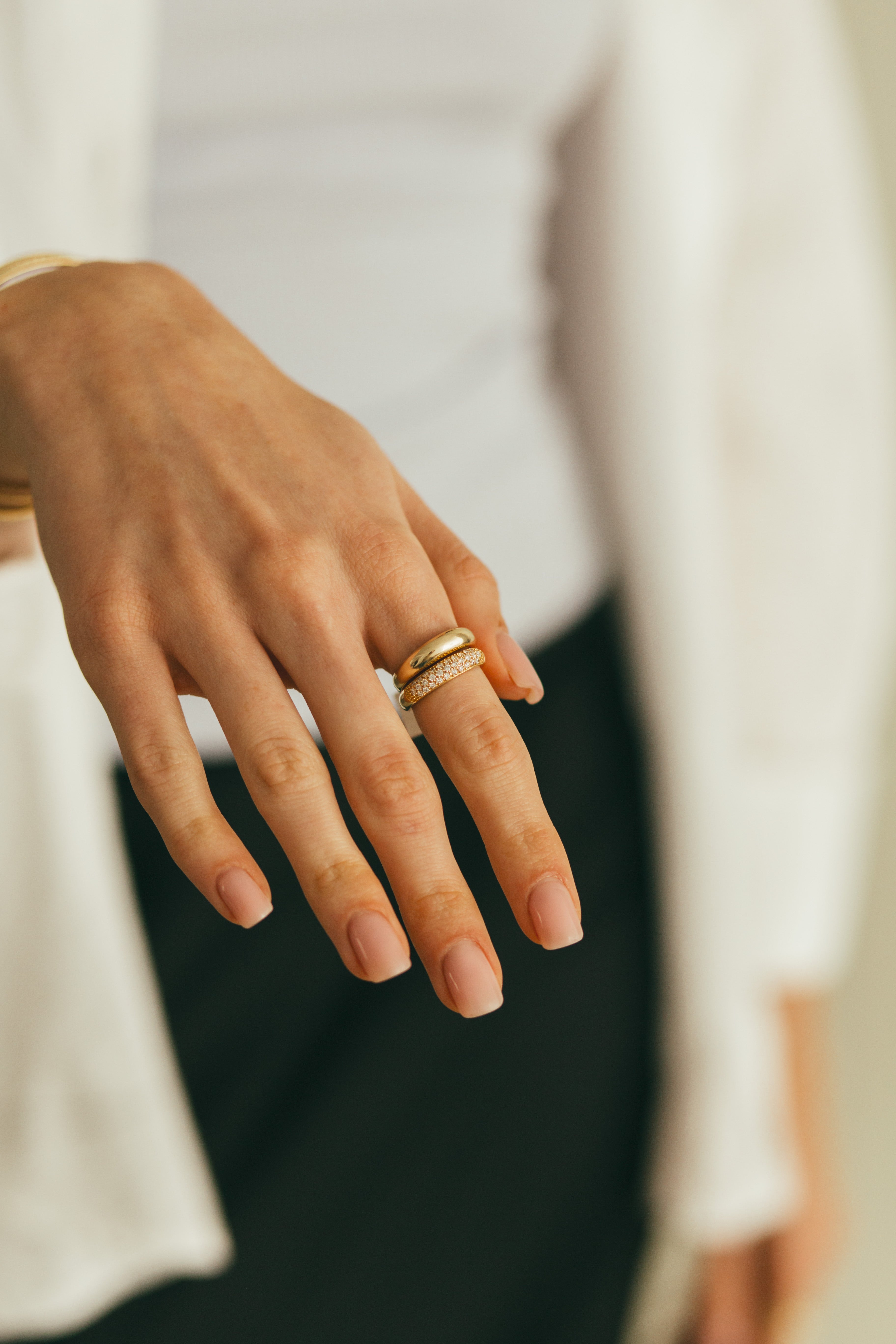 Close-up of a hand wearing a gold diamond dome ring with sparkling diamonds on a neutral background.