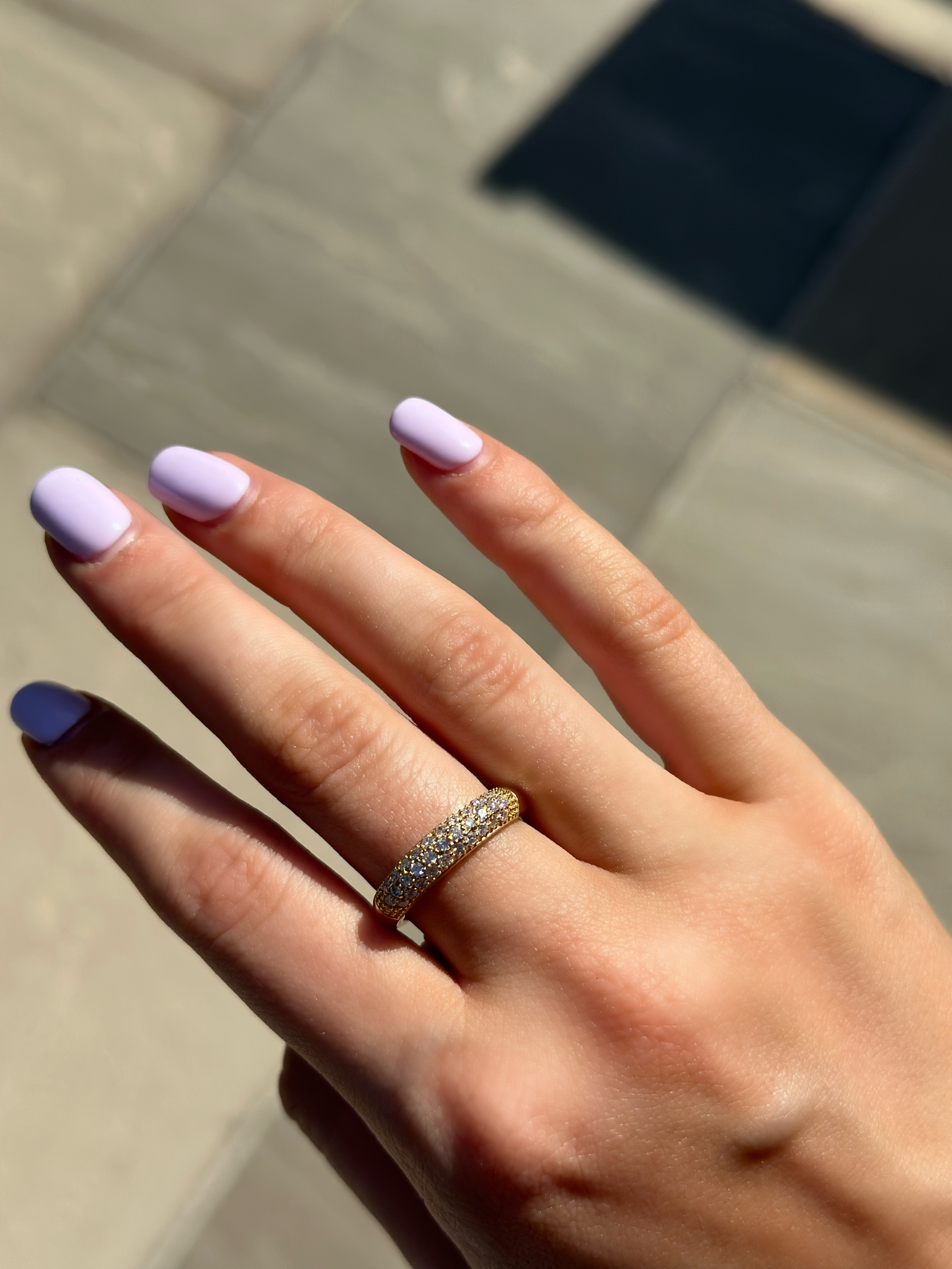 A close-up of a hand wearing a gold diamond dome ring with sparkling diamonds catching the sunlight.