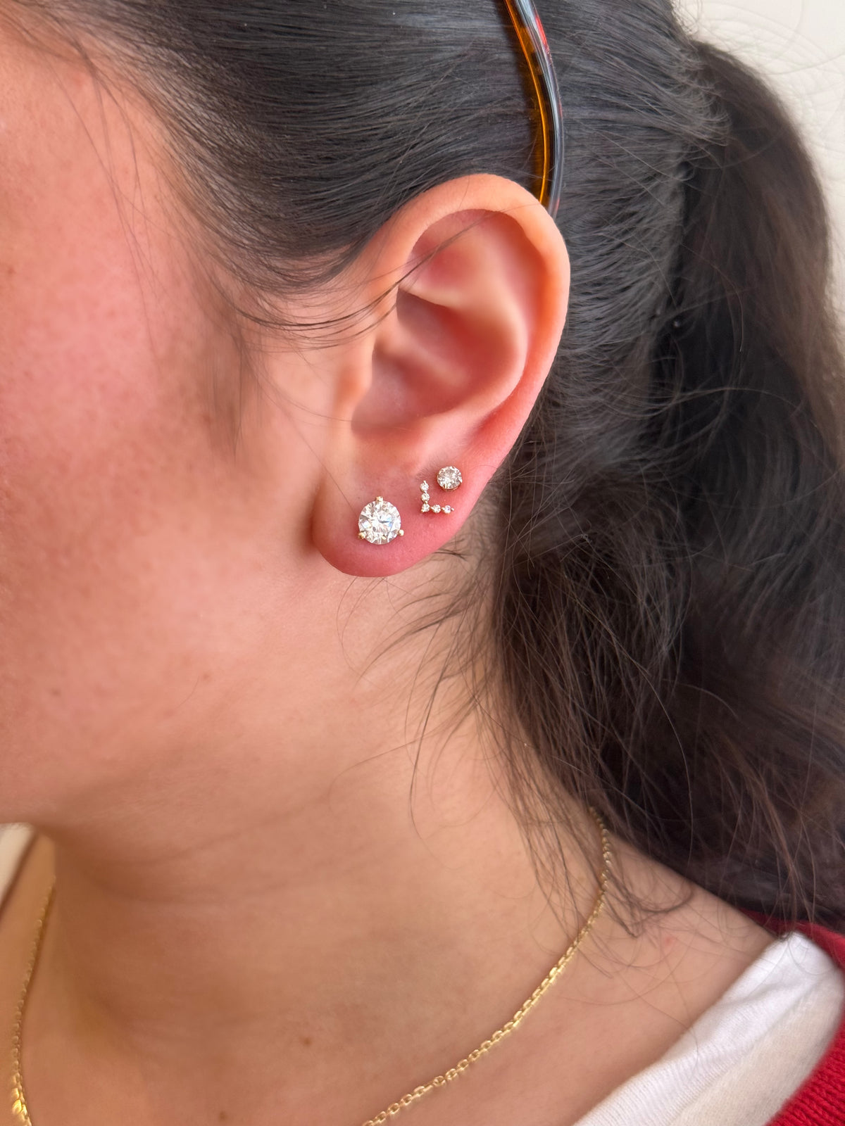 Close-up of a person's ear wearing three diamond stud earrings.