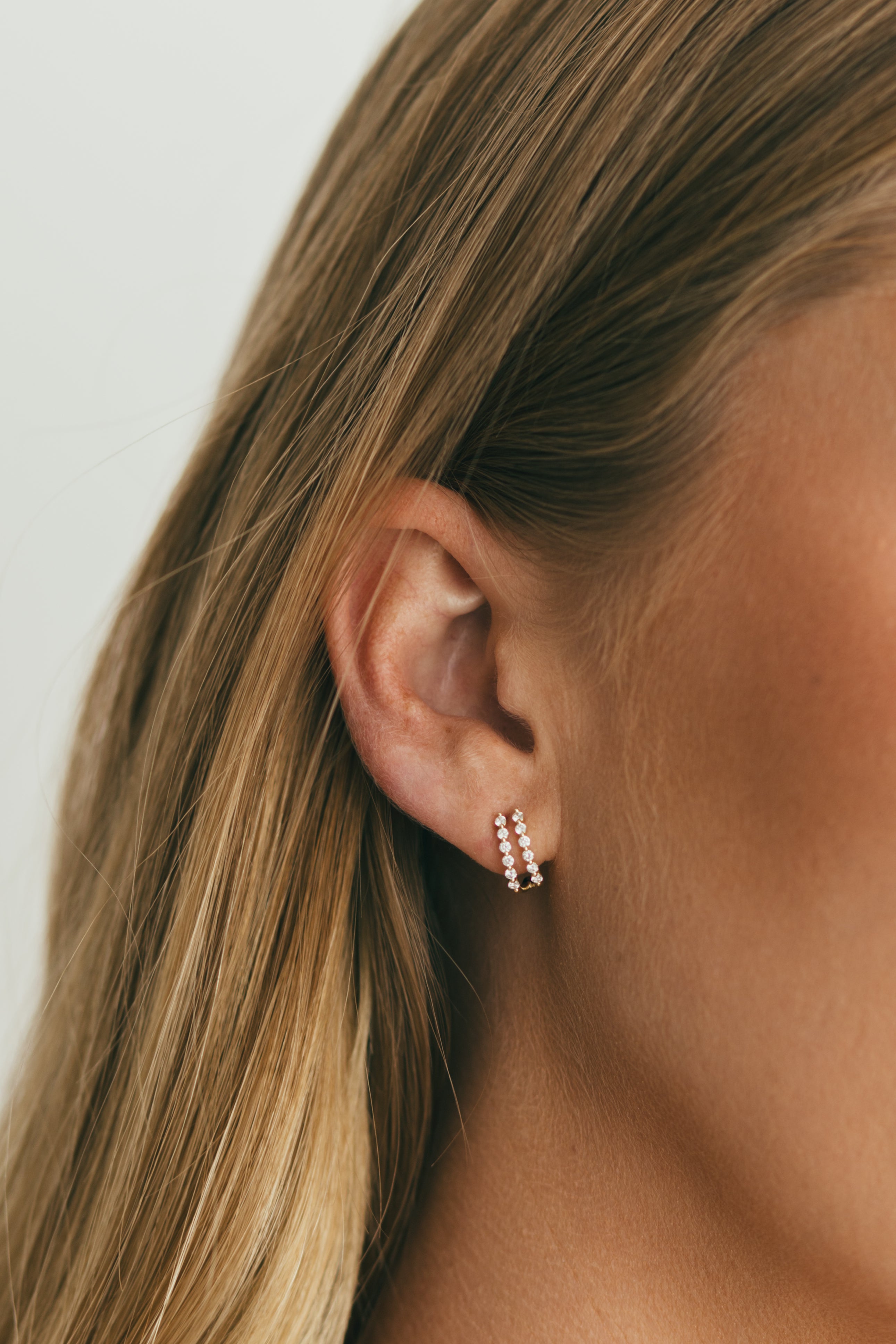 close up of ear displaying gold single prong double diamond huggies 