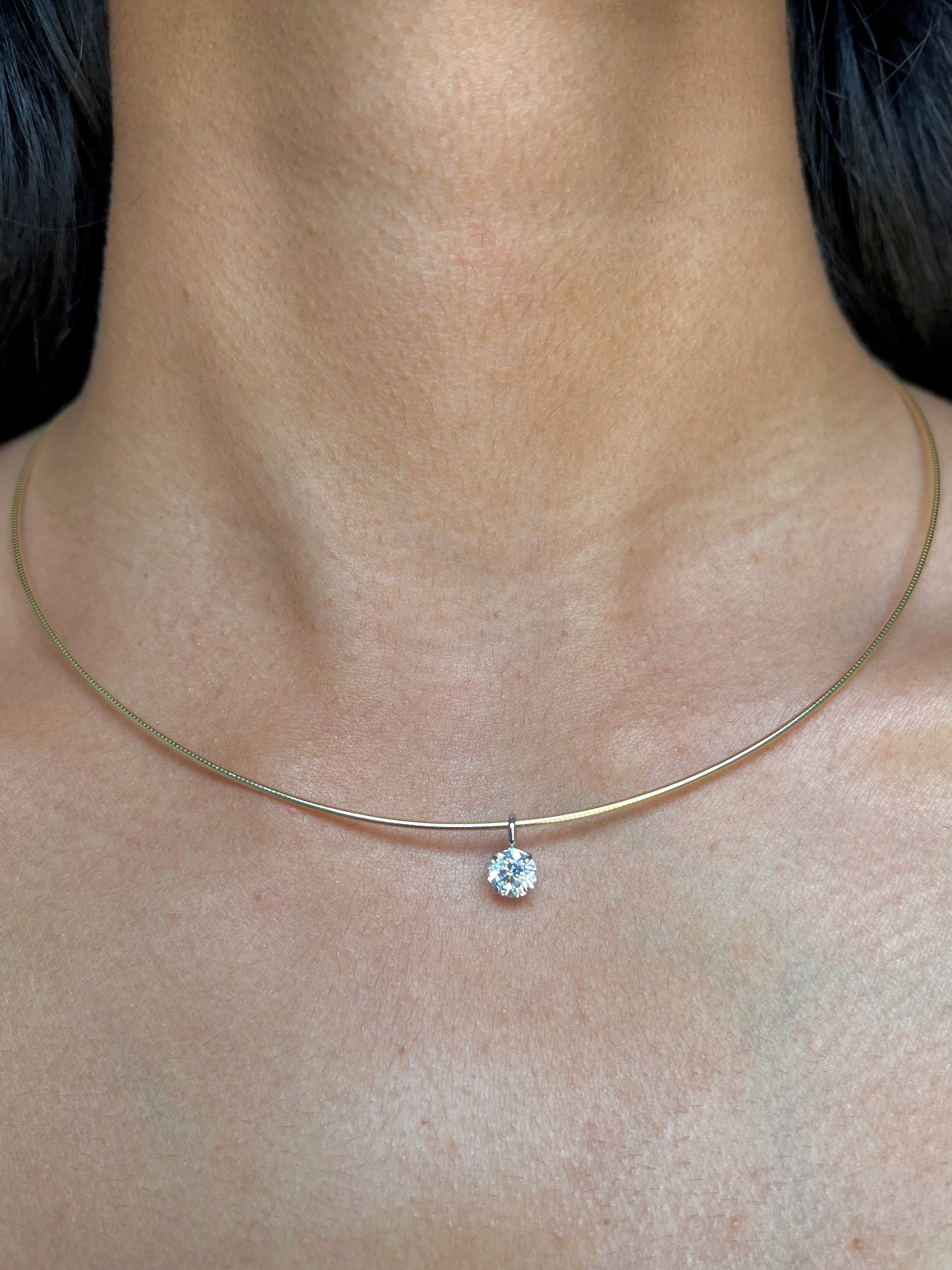 A person's neck wearing a solid gold wire necklace with a beautiful floating diamond round pendant.