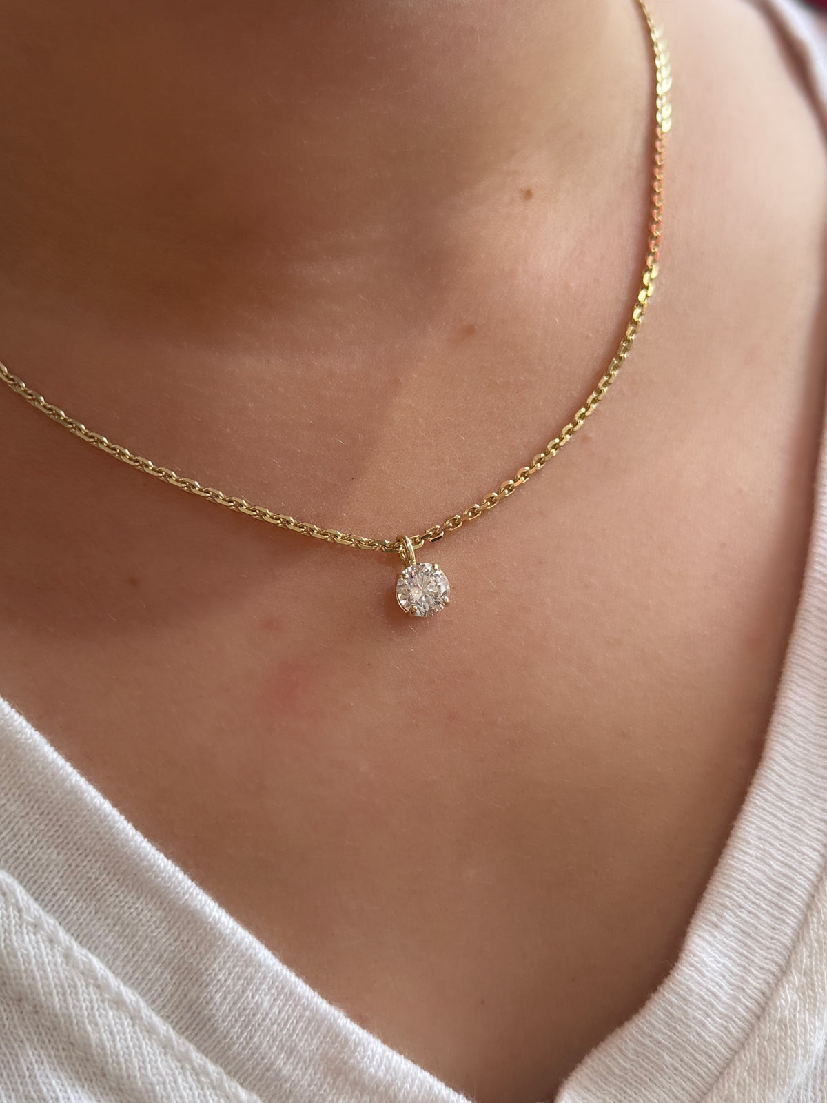 Gold necklace with a diamond pendant worn by a person in a white top.