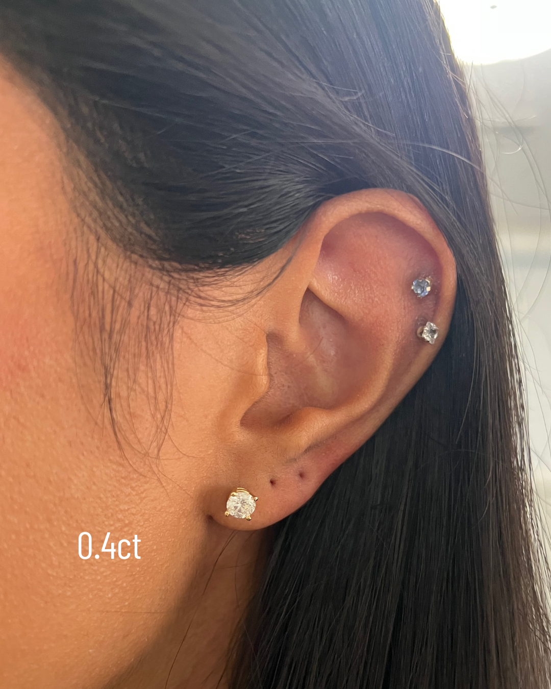 Close-up of an ear wearing a diamond stud earring with '0.4ct' label.
