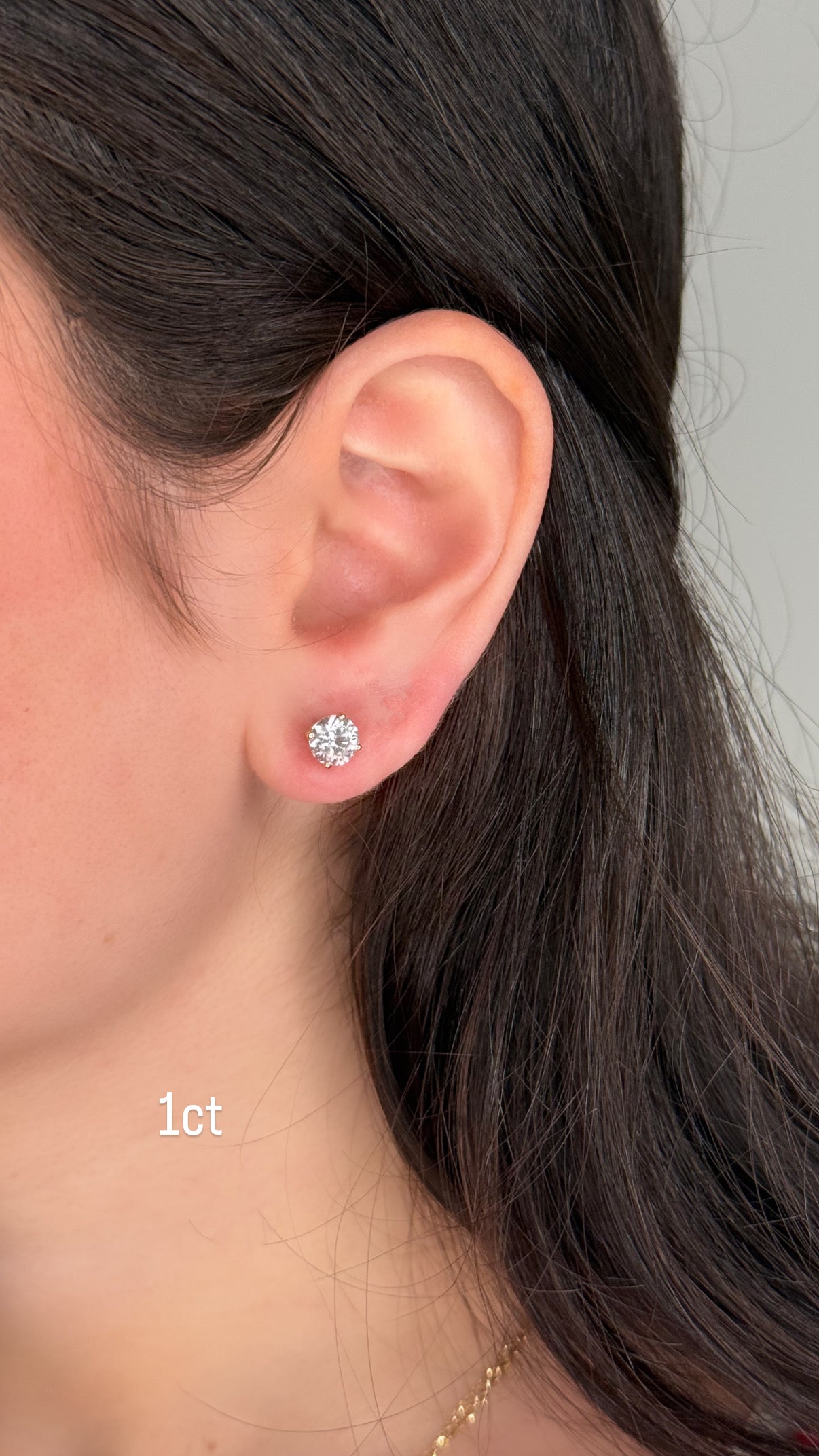 Close-up of an ear wearing a diamond stud earring with '1ct' label.