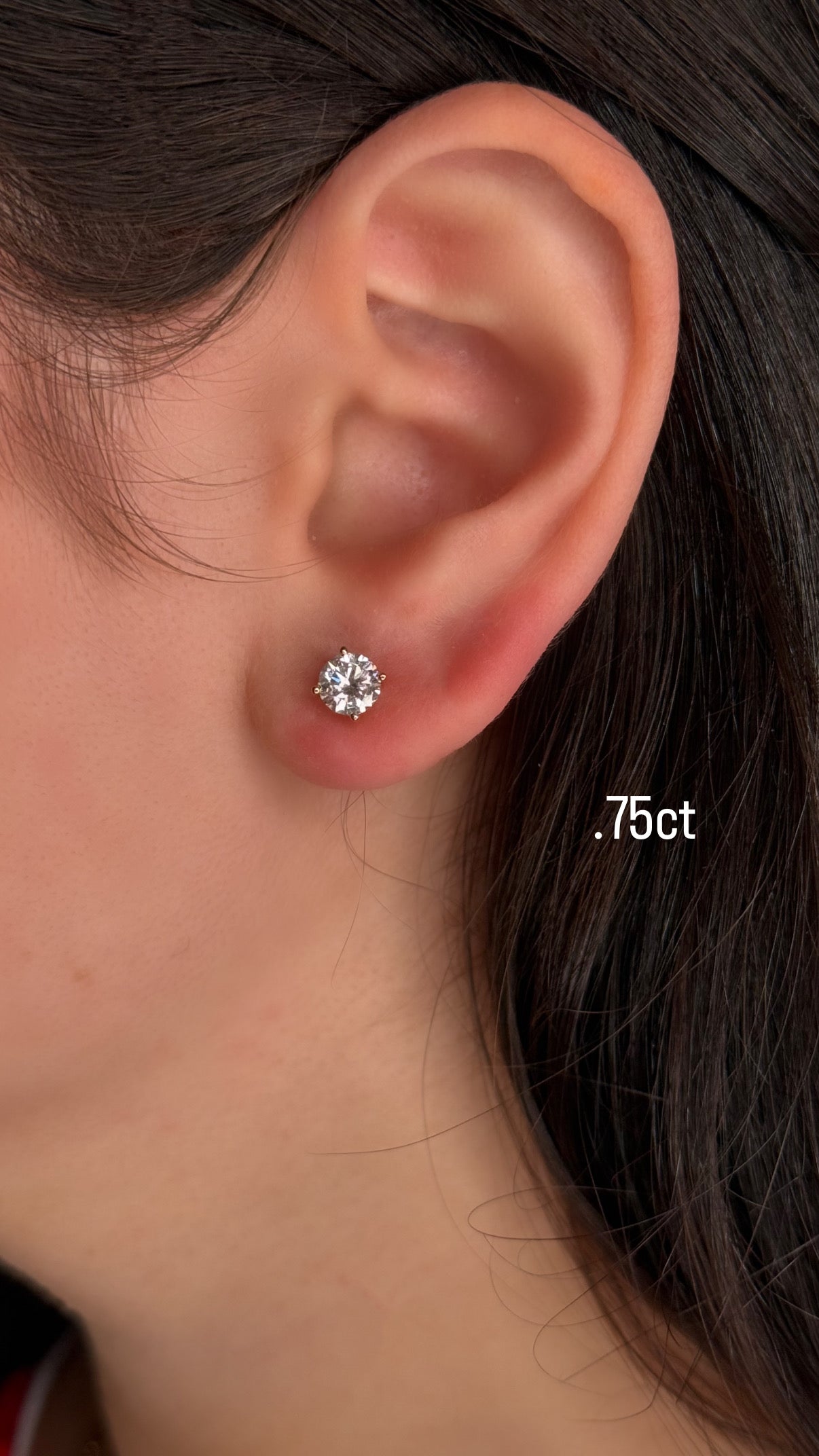 Close-up of an ear wearing a diamond stud earring with '0.75ct' text.