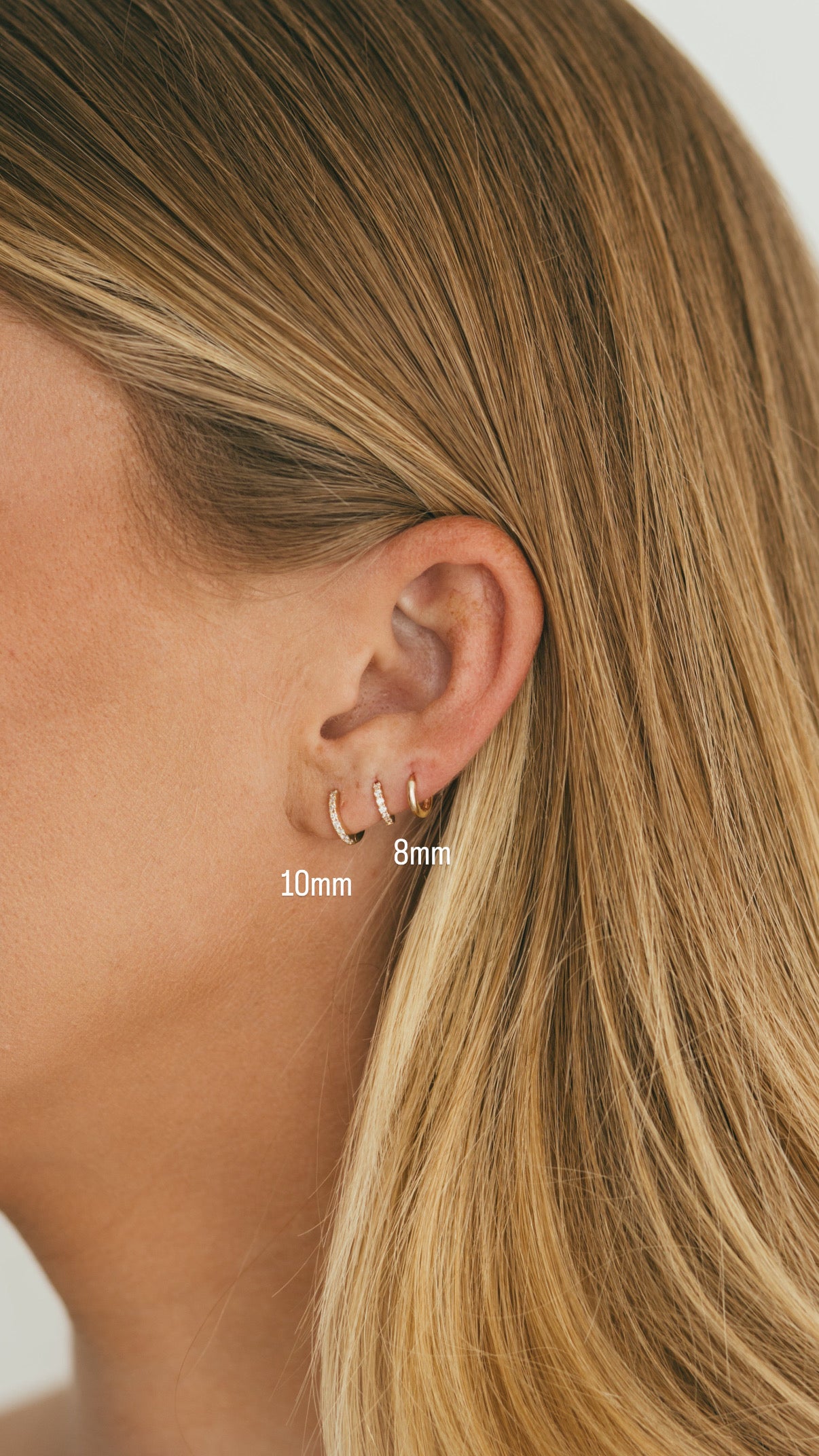 Close-up of an ear wearing two gold hoop earrings with size labels.