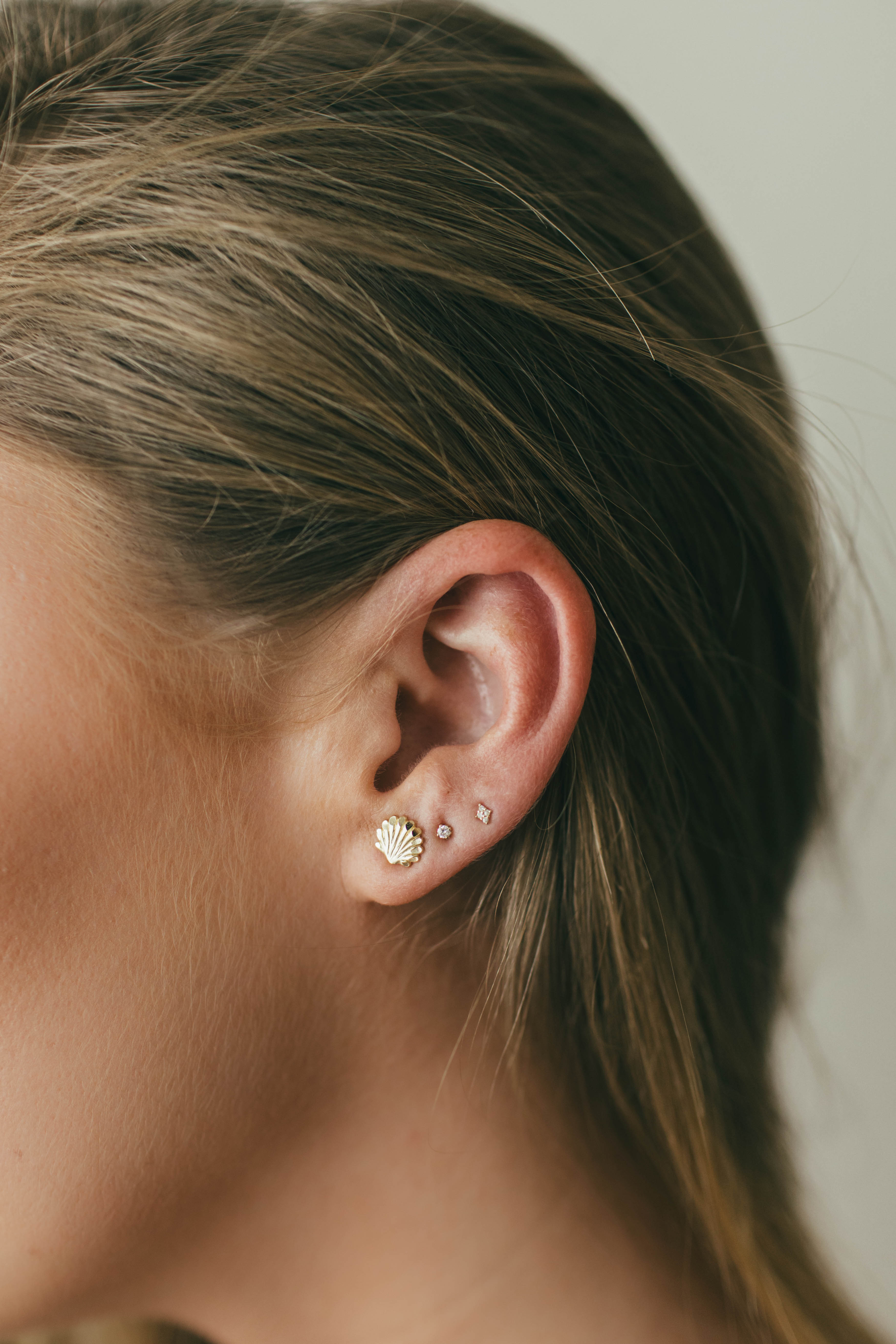 Close-up of an ear wearing gold earrings with a neutral background