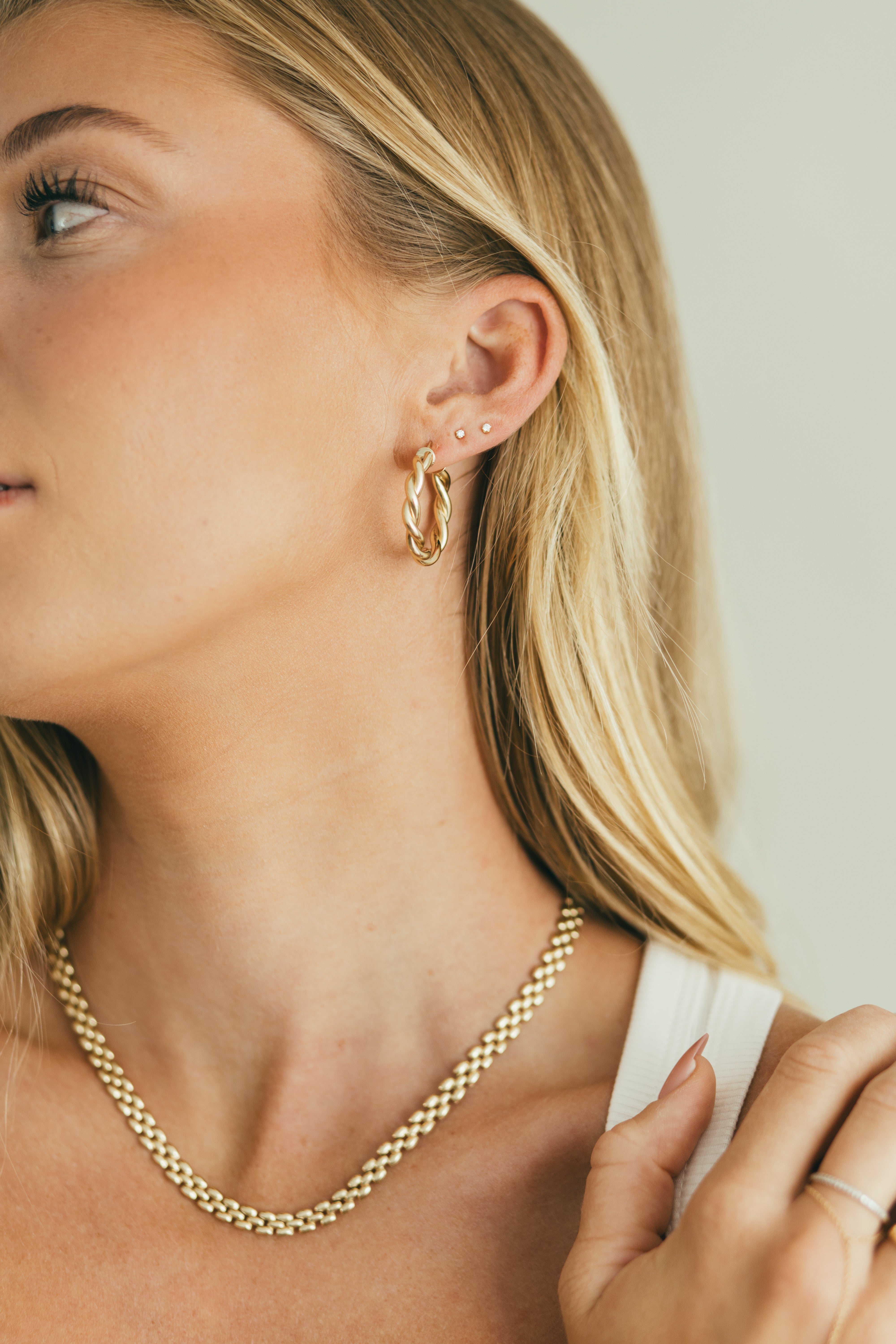 Close-up of a woman wearing gold hoop earrings and a gold chain necklace.