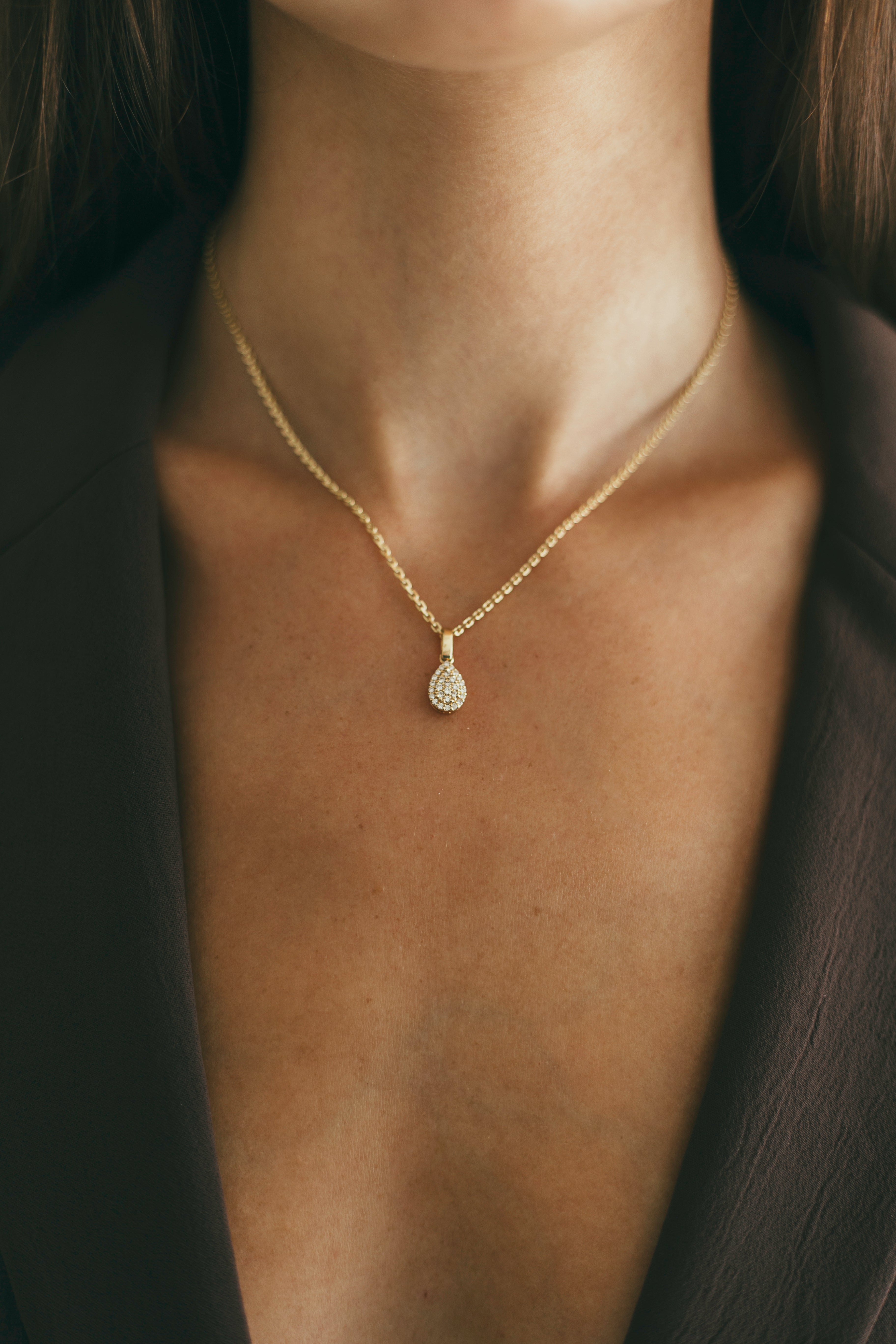 Gold necklace with a pendant on a person's neck against a dark background