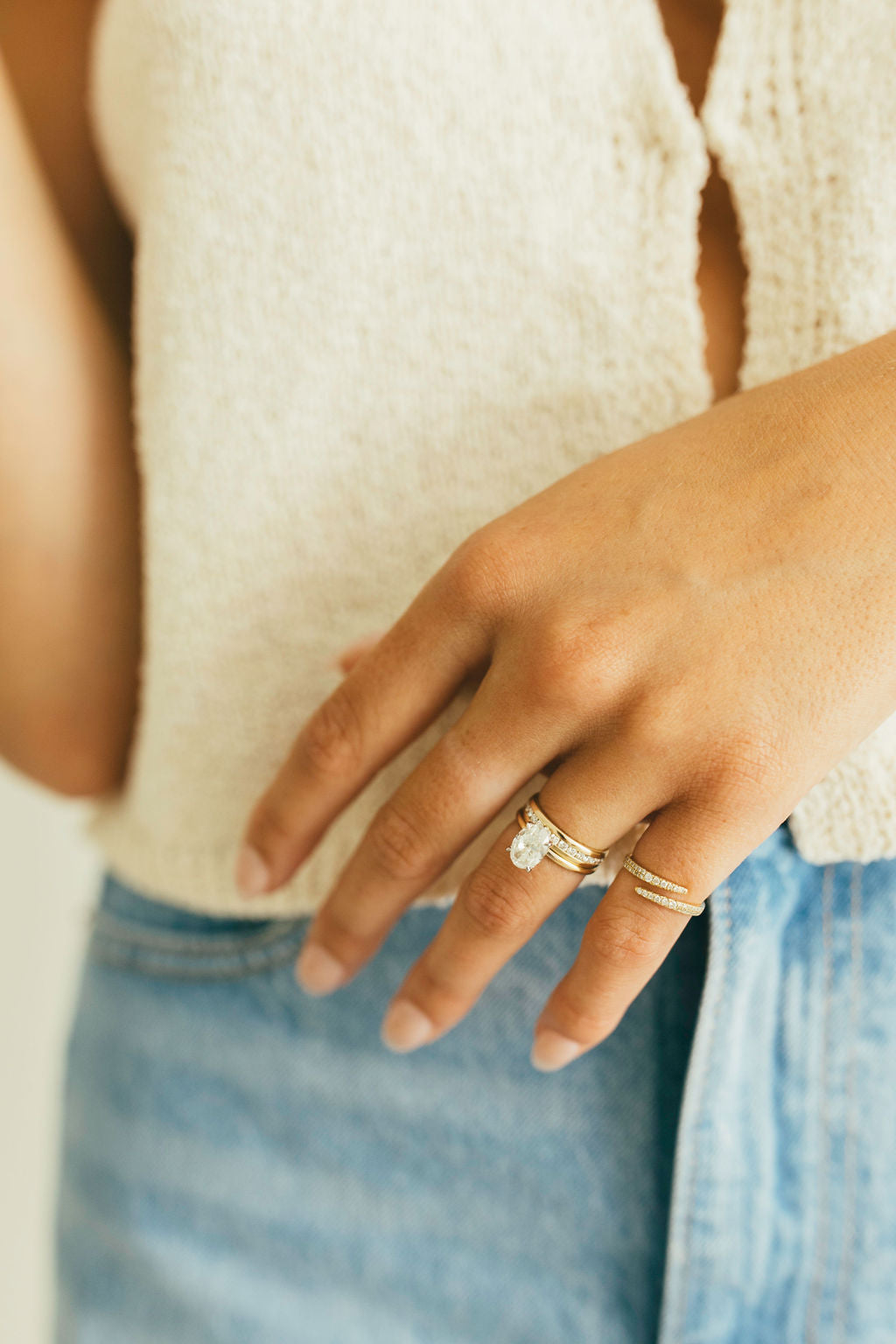 Multiple gold rings styled on a person's hand against a soft button up top and light denim jeans.