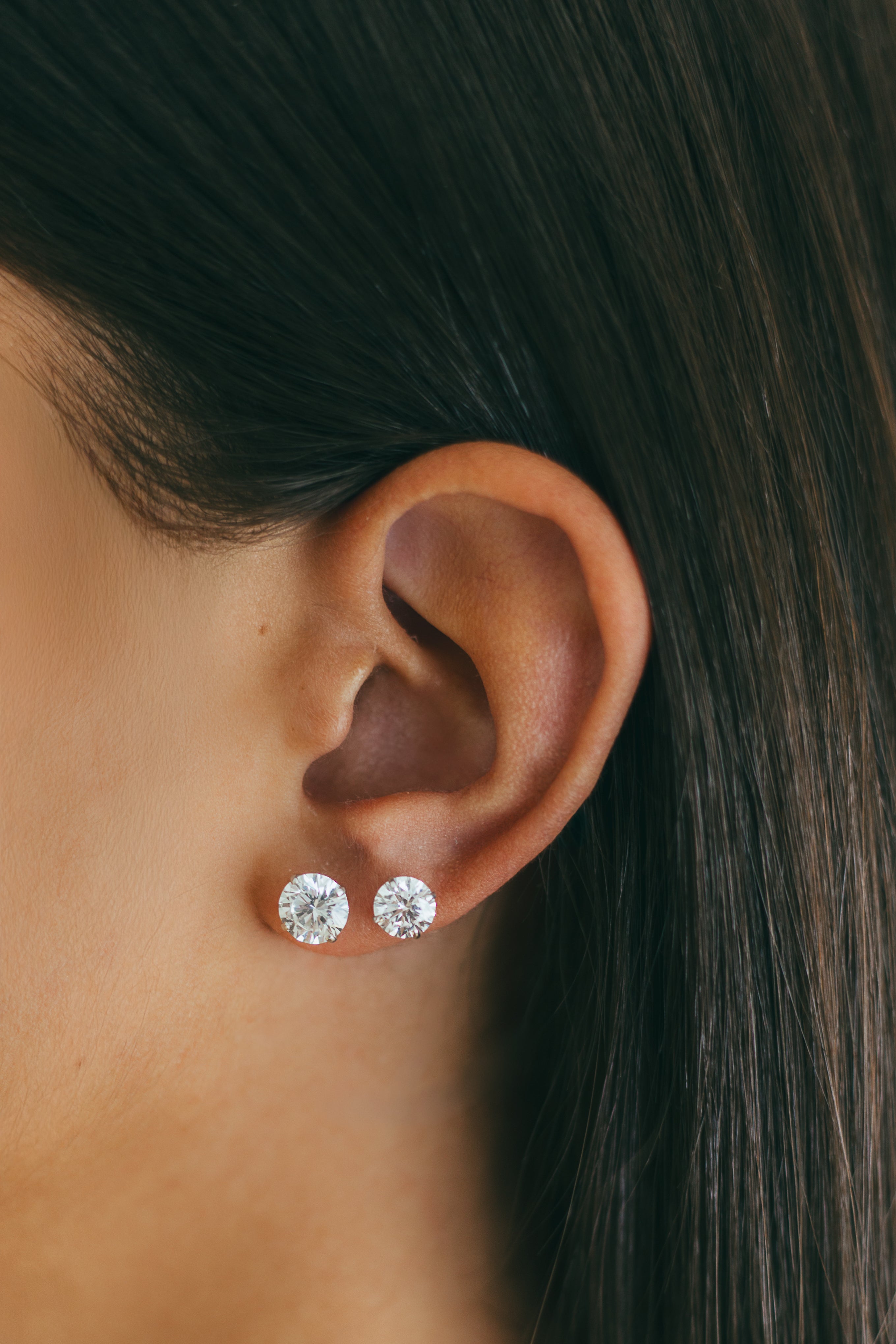 Close-up of an ear wearing two diamond stud earrings with dark hair in the background.