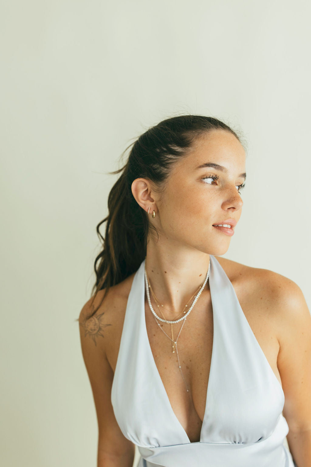Woman wearing a light blue halter top, gold earrngs, and a tennis necklace against a plain background